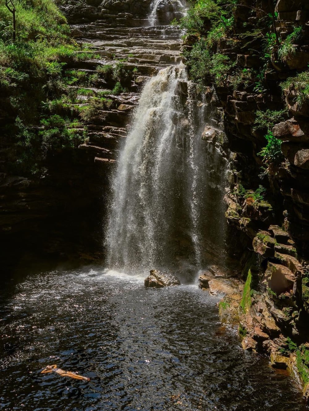 Una persona nuota nella piscina naturale scura e tranquilla alla base della cascata do Sossego, alta 20 metri, vicino a Lençóis. Una persona nuota nella piscina naturale scura e tranquilla alla base della cascata do Sossego, alta 20 metri, vicino a Lençóis.