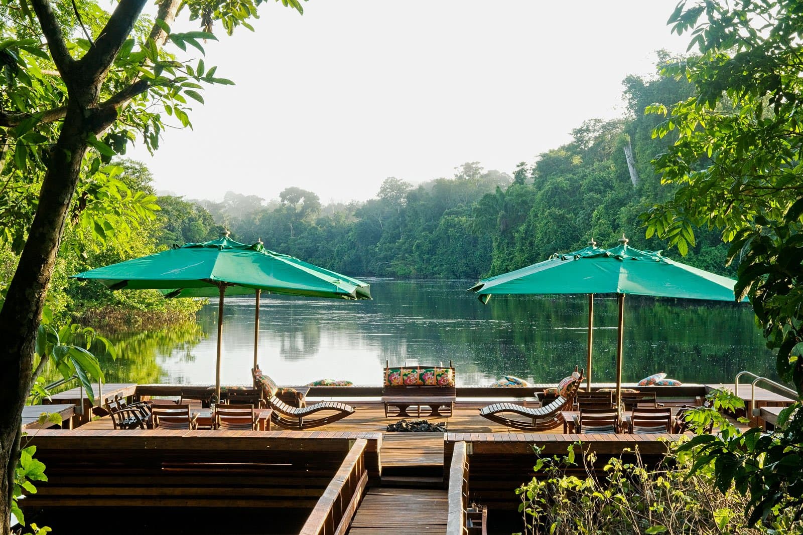 Le feu de camp, la rivière, la forêt qui respire. La soirée commence ici. Photo: Luis Gomes Une terrasse en bois avec des chaises longues en teck et des parasols verts domine une rivière aux eaux sombres encadrée par la forêt amazonienne, parfaite pour l'observation des oiseaux en Amazonie entre deux excursions.