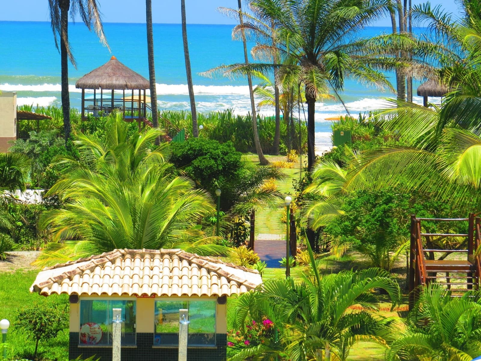 Palmengarten vorne, Atlantik hinten, der perfekte Start in eine Radtour. Üppiger Tropengatten mit Palmen und einem Ziegel-Kiosk, der über einen Backsteinweg zu einem Strand-Pavillon mit Strohdach und dem Atlantik führt — ideale Basis für eine Bahia-Radreise