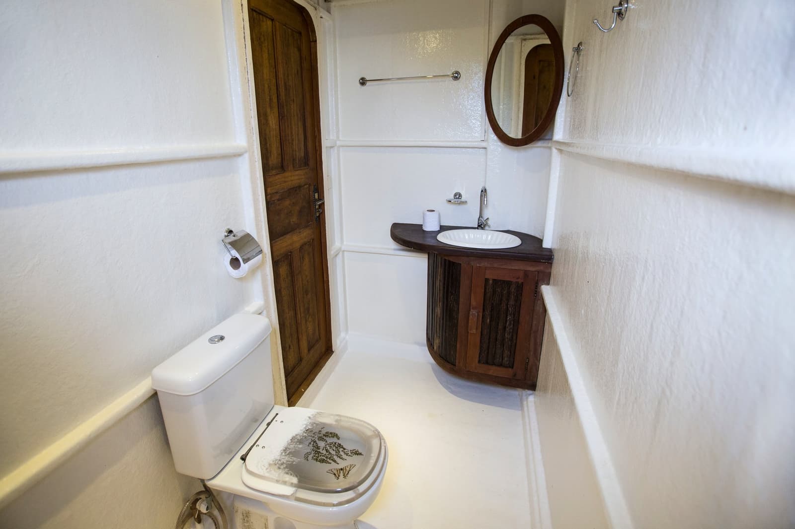 Wenig Platz, viel Idee, auch auf dem Fluss lässt es sich gut aushalten. Kompaktes Privatbad auf einer Amazonas-Kreuzfahrt in Brasilien mit weißer Toilette, geschwungenem Holzunterschrank, rundem Waschbecken, ovalem Spiegel und einer massiven Holztür