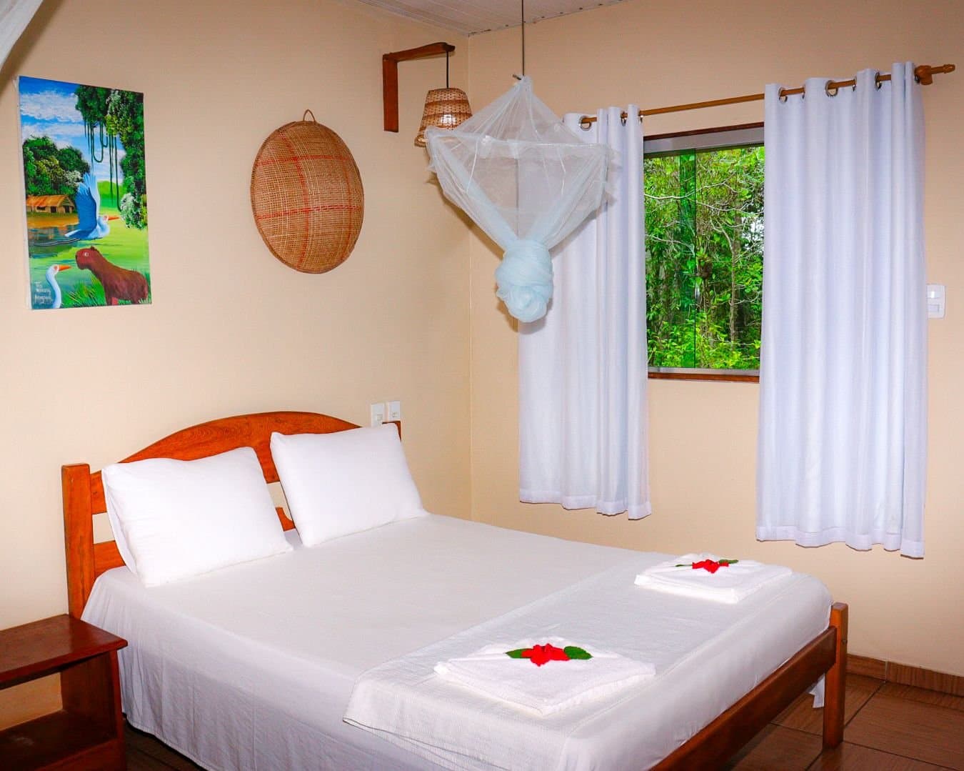 Gefaltete Handtücher, frische Blumen und draußen der Urwald. Gute Nacht. Ein gemütliches Zimmer im Amazon Turtle Lodge mit Holzbett, weißem Moskitonetz-Baldachin, roten Hibiskusblüten auf gefalteten Handtüchern und Blick auf den grünen Regenwald