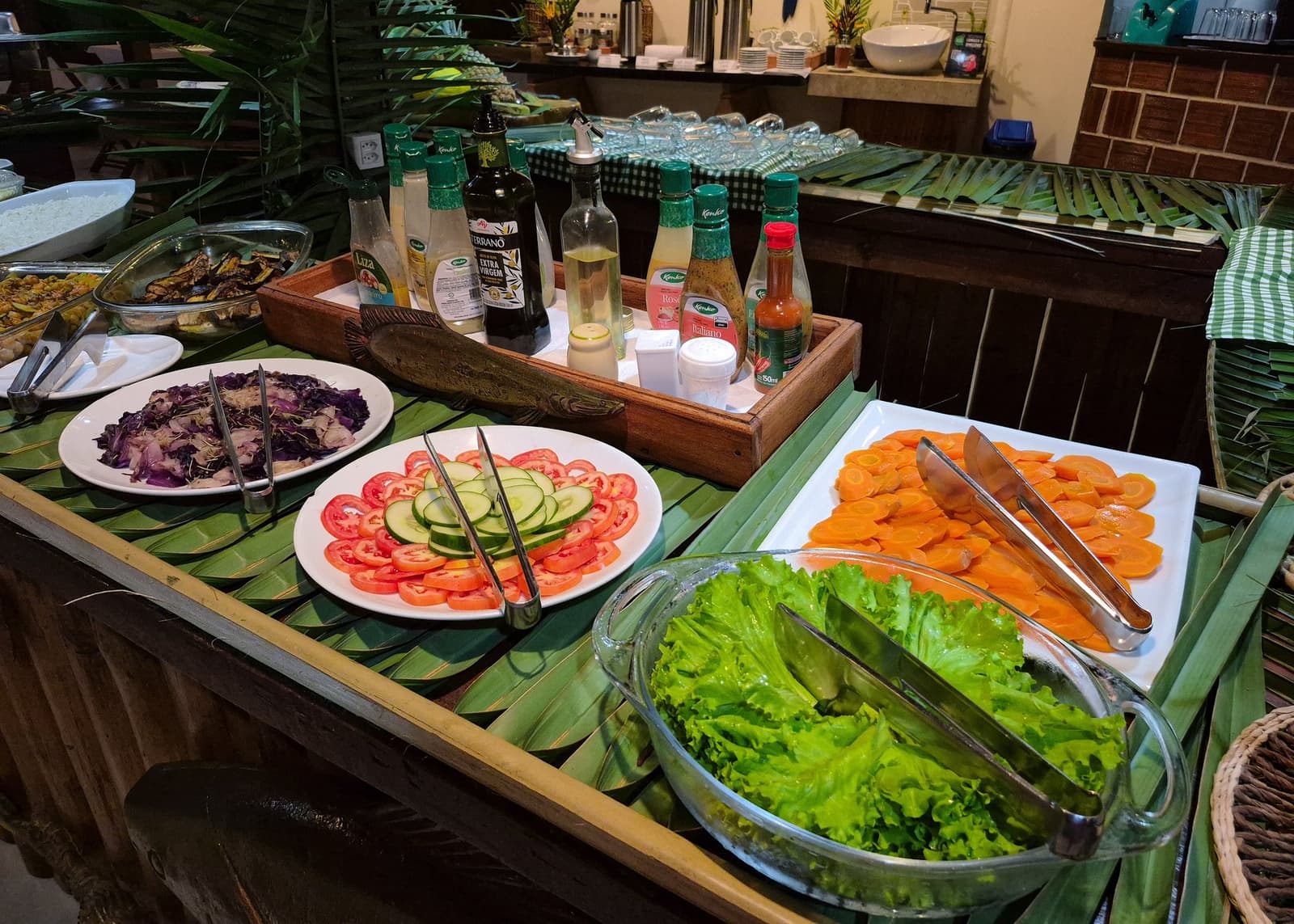 Im Dschungel gut essen, kein Problem, wenn die Lodge weiß, was sie tut. Ein farbenfrohes Salatbuffet im Amazon Turtle Lodge mit Tellern mit geschnittenen Tomaten, Gurken, Karotten, Rotkohl und frischem Salat, angerichtet auf Bananenblättern neben Dressings und Olivenöl