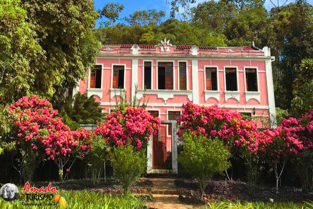 Eine Kakaofarm, deren Garten schon die Anreise rechtfertigt. Rosafarbenes zweistöckiges Kolonialgebäude der Fazenda Vila Rosa, umgeben von blühenden Bougainvilleen und üppigem Atlantischen Regenwald auf der Bahia-Radroute