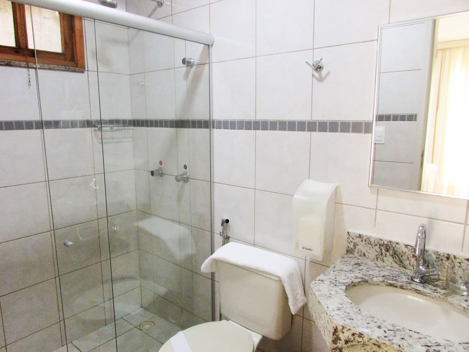 Nach 30 km im Sattel schmeckt die heiße Dusche besonders gut. Sauberes Privatbadezimmer in einer Unterkunft der Bahia-Radtour mit Glasdusche, Granitwaschbecken und weißen Kacheln mit dekorativem Bordürenstreifen