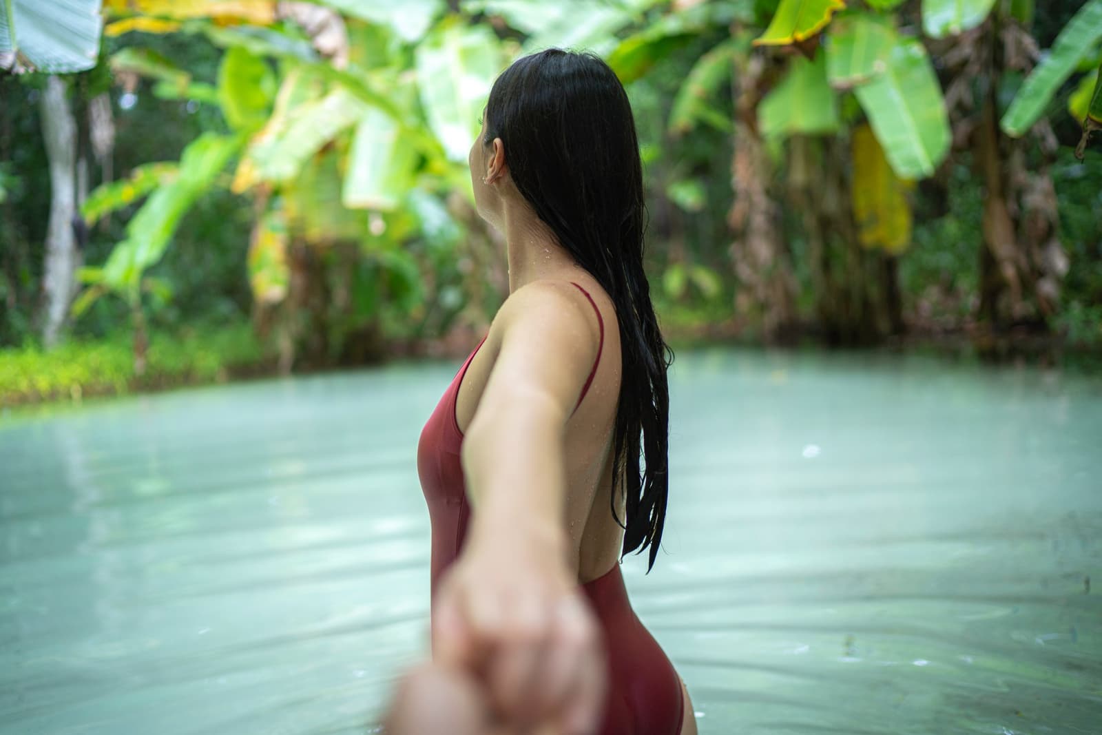 Kühles Wasser, kein Grund unter den Füßen, der Fervedouro hält einen ganz von selbst oben. Photo: FG Trade Eine Frau im roten Badeanzug steht hüfttief in einer klaren, milchig-blauen Naturquelle umgeben von dichter tropischer Vegetation beim Jalapão-Trekking und streckt ihre Hand zur Kamera aus