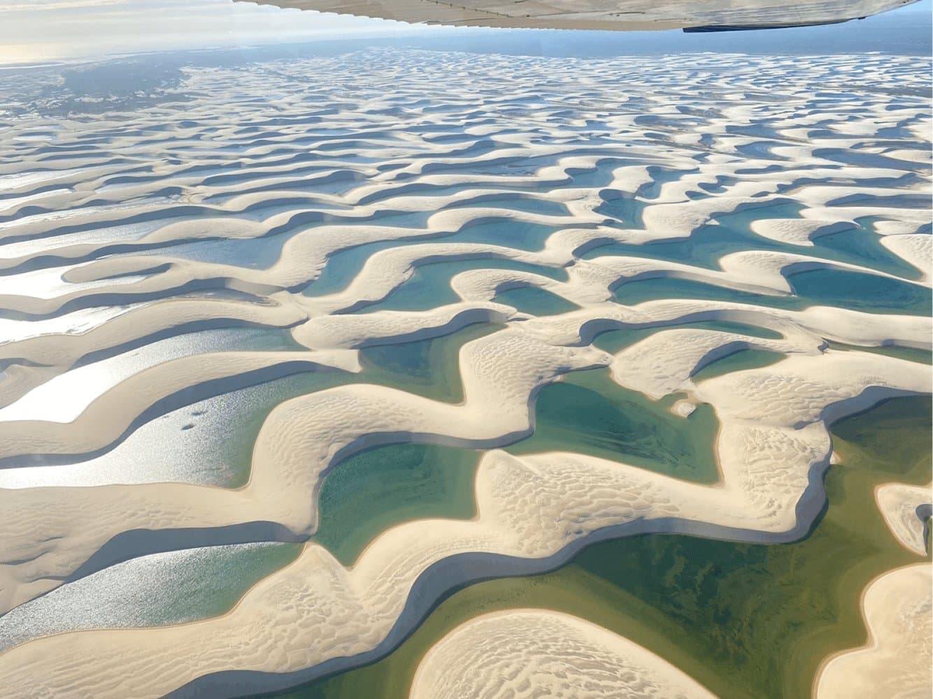 Aus der Luft wirkt die Landschaft wie ein Muster, das die Natur ganz beiläufig entworfen hat. Luftaufnahme aus einem Kleinflugzeug über den weißen Sanddünen und türkisfarbenen Lagunen des Lençóis Maranhenses, die sich bis zum Horizont erstrecken