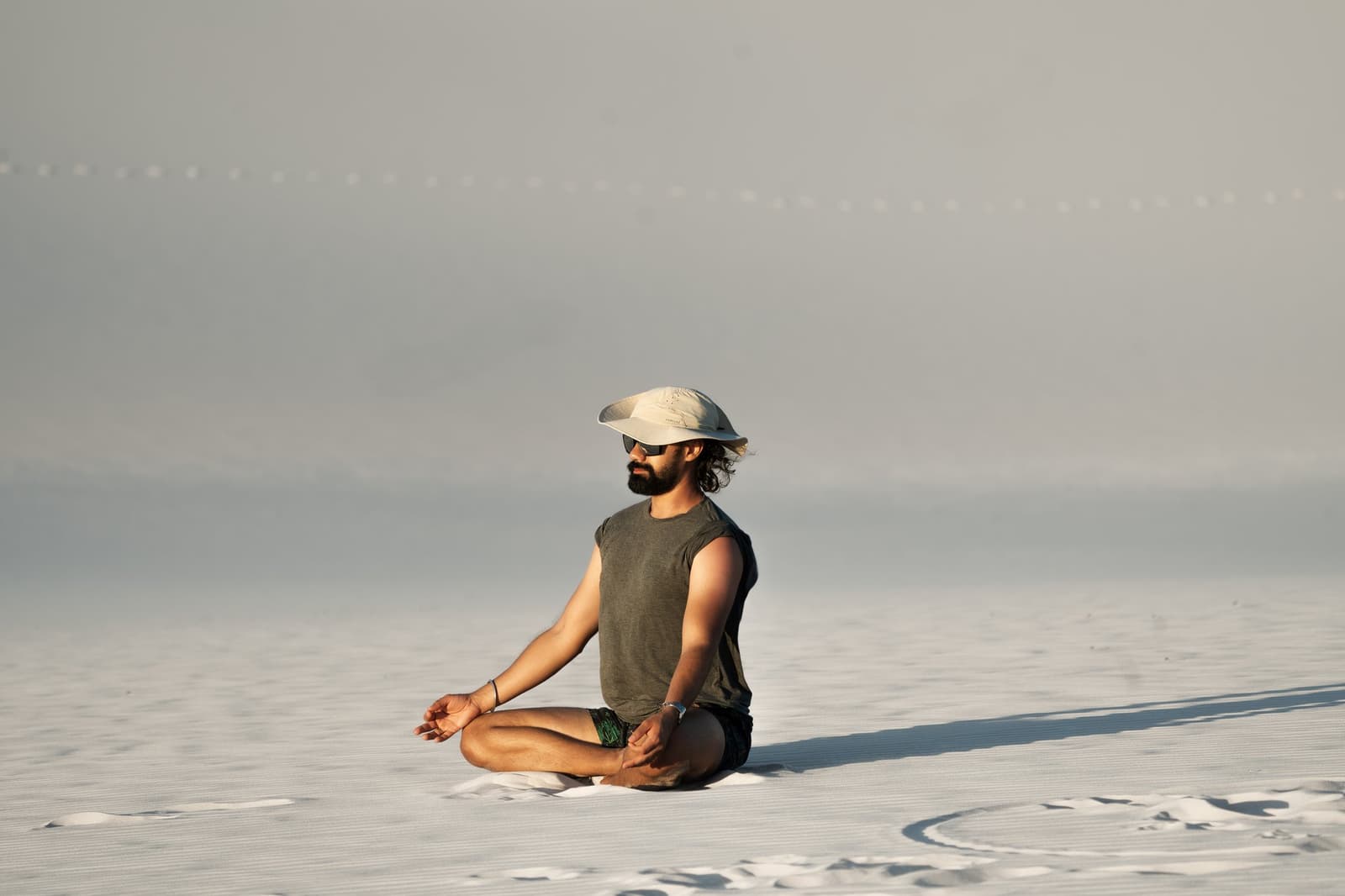 Hier findet man die Stille, die man in der Stadt vergeblich sucht. Ein bärtiger Mann mit Kappe und Sonnenbrille sitzt im Lotussitz auf den weitläufigen weißen Sandflächen der Lençóis Maranhenses, der dunstige Horizont weit hinter ihm