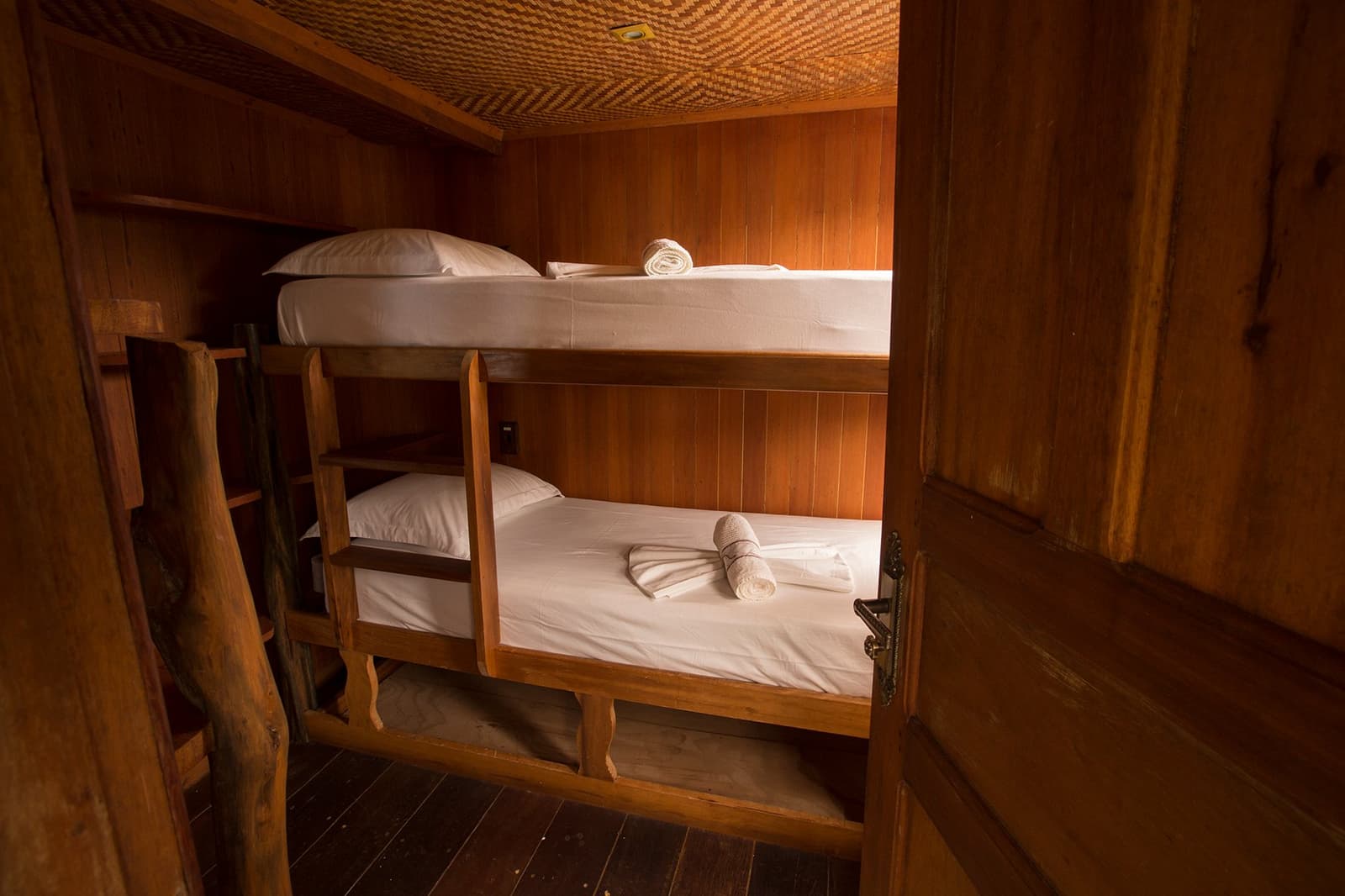 Klein, ordentlich und nah am Fluss, mehr braucht es nicht. Etagenbett aus Holz mit weißer Bettwäsche und gerollten Handtüchern in einer gemütlichen Kabine des Amazonas-Kreuzfahrtschiffs, mit warmen Holzpaneelen und geflochtenem Deckendekor
