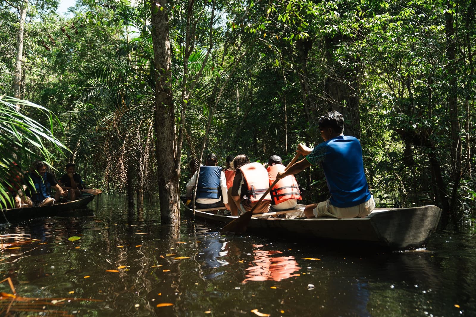 Der Wald zeigt sich von seiner stillen Seite, wenn man nur Zentimeter über dem Wasser sitzt. Gäste mit Schwimmwesten paddeln in Einbaumkanus durch einen überfluteten Igapó-Urwald beim Amazon Turtle Lodge Ausflug
