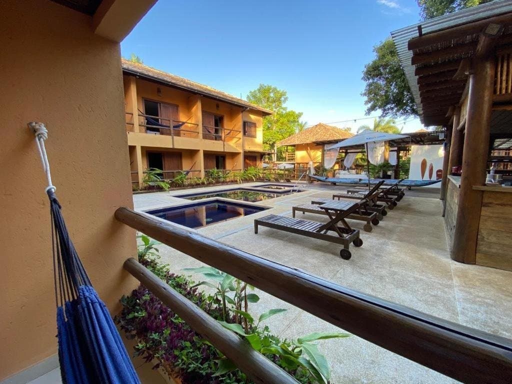 Pool, Hängematte, und kein Plan für den Rest des Abends. Blick von einem Balkon mit blauer Hängematte auf den Pool, Liegestühle und den zweistöckigen Innenhof einer Pension auf einer Radtour durch Bahia in Itacaré