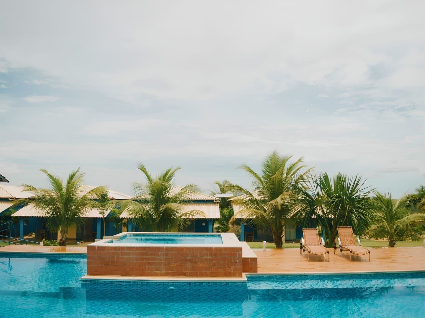 Kaltes Wasser, warmer Abend, kein Empfang. Genau der Plan. Außenpool mit erhöhtem Jacuzzi und zwei Liegestühlen auf einer gefliesten Terrasse, Palmen und blau gestrichene Bungalows im Hintergrund einer Unterkunft in Jalapão