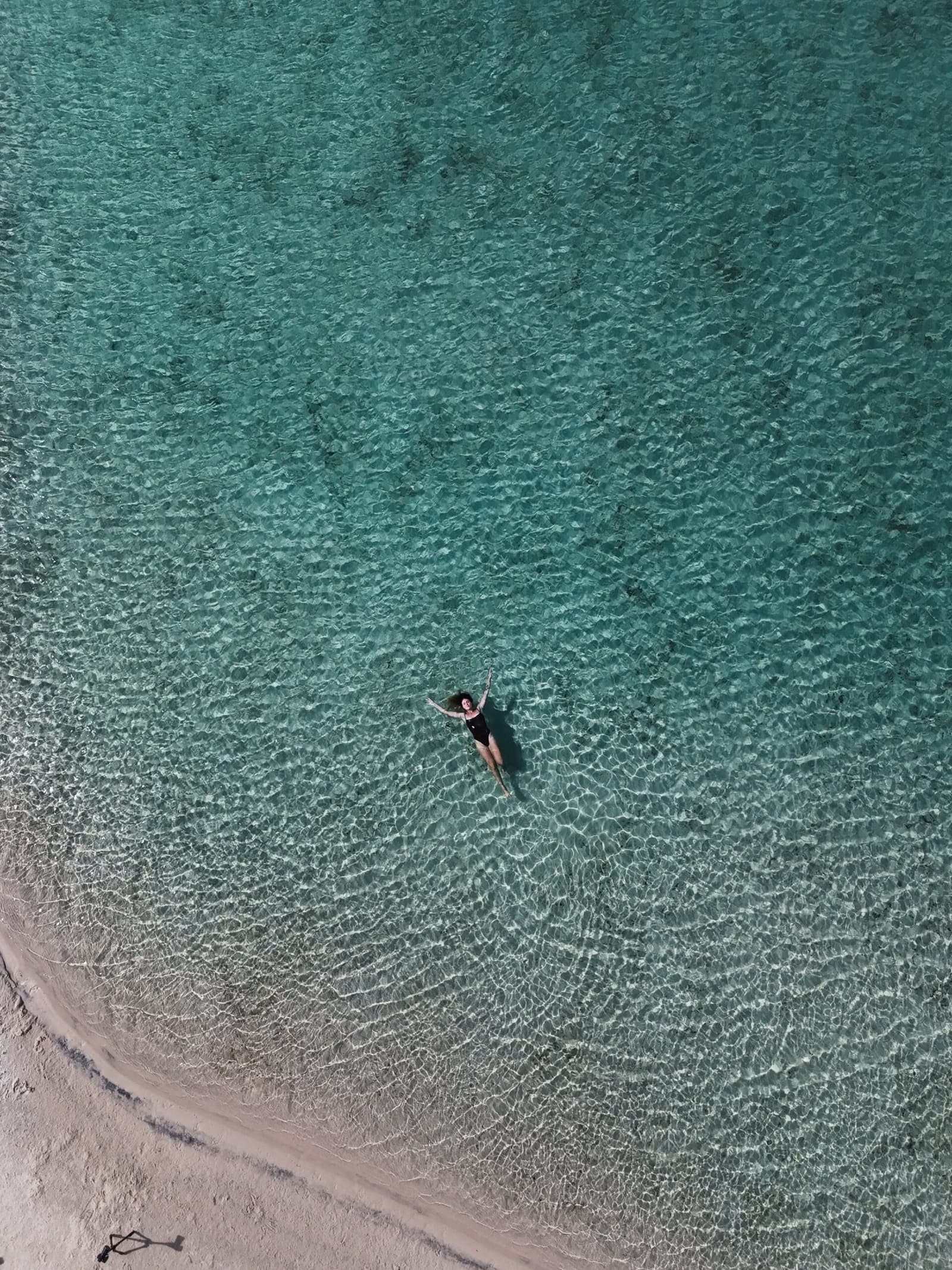 So klar, dass man kaum glaubt, es ist Wasser und kein Glas. Luftaufnahme einer Frau, die auf dem Rücken in flachem türkisfarbenem Wasser nahe einem weißen Sandstrand im Lençóis Maranhenses treibt