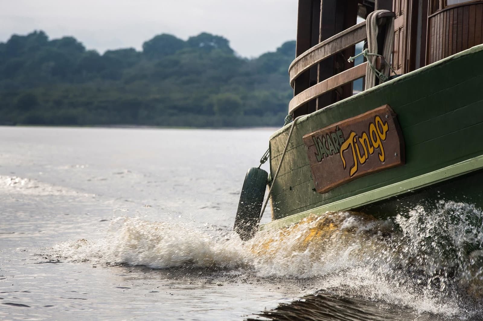 Der Jacaré Tingo kennt jeden Meter dieses Flusses. Der Bug des Flussboots Jacaré-Açu pflügt durch das dunkle Amazonaswasser mit weißer Gischt, dichter Regenwald am gegenüberliegenden Ufer sichtbar