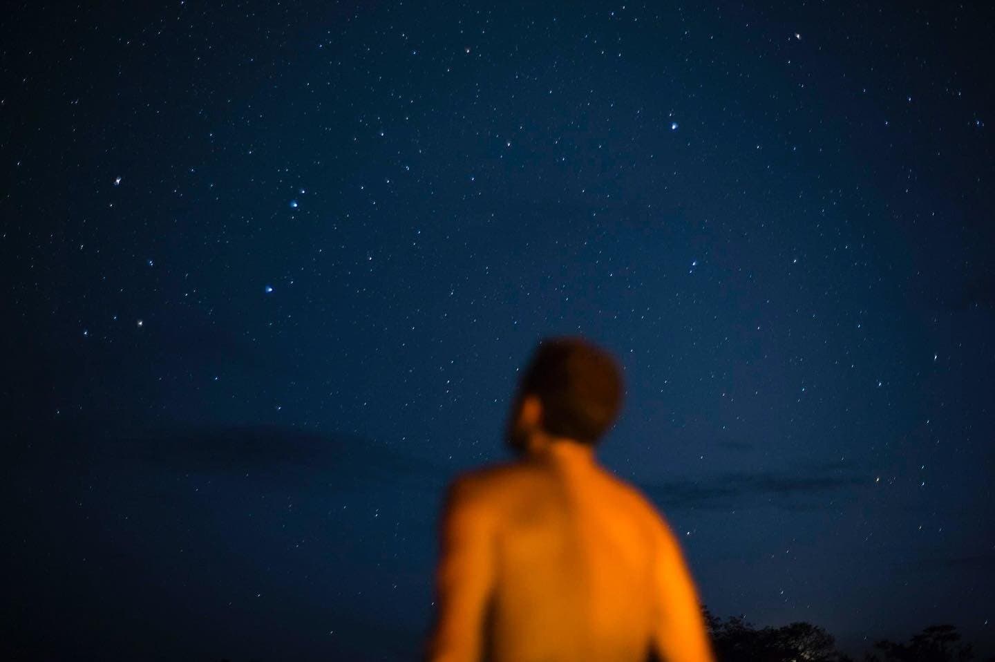 Kein Stadtlicht, keine Ablenkung. Nur du und der Südhimmel in seiner ganzen Breite. Eine vom warmen Feuerschein beleuchtete Person beobachtet einen funkelnden Sternenhimmel während einer Amazon-Dschungelkreuzfahrt in Brasilien