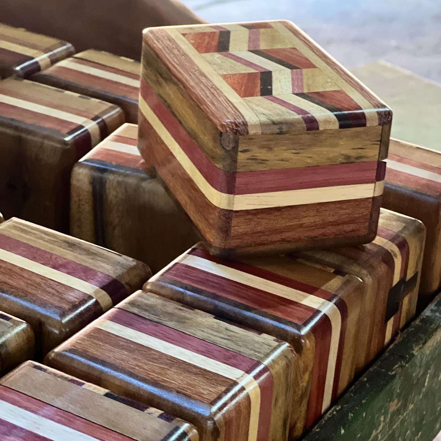 Kein Kasten wie der andere, jede Maserung erzählt ihre eigene Geschichte. Sammlung kleiner handgefertigter Holzkästchen mit eingelegten Streifenmustern in warmen Rot-, Creme- und Dunkelbrauntönen aus verschiedenen Holzarten, präsentiert auf einem Tablett bei einem Handwerks-Workshop