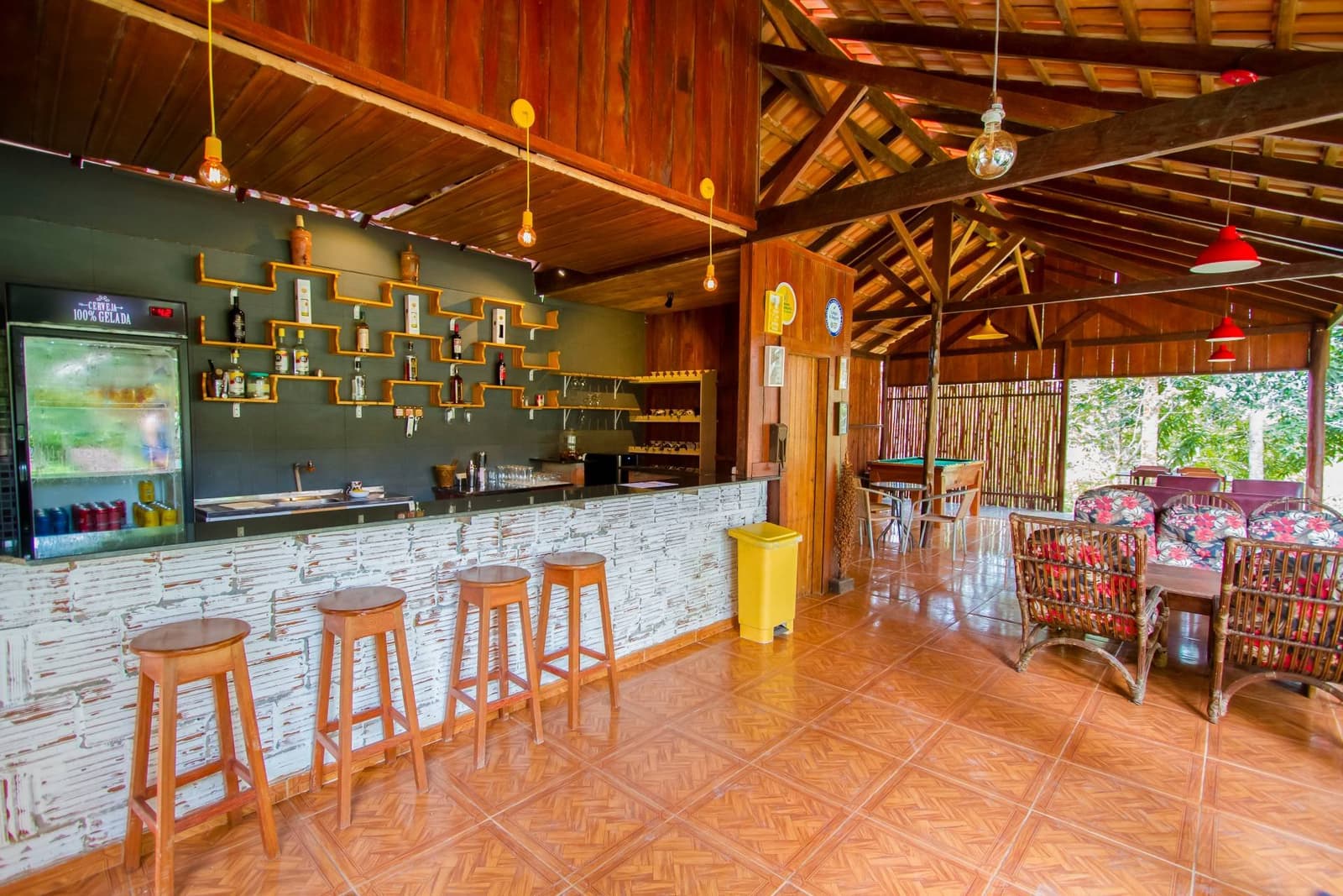 Kühles Getränk, Holzhocker, Dschungel nebenan. Besser kann ein Flusstag nicht enden. Die Open-Air-Bar der Amazon Turtle Lodge mit einer weiß verputzten Steinbar, Holzhockern, gestaffelten Flaschenregalen und einem hohen Holzbalkengewölbe, das den Blick auf üppiges Grün freigibt.