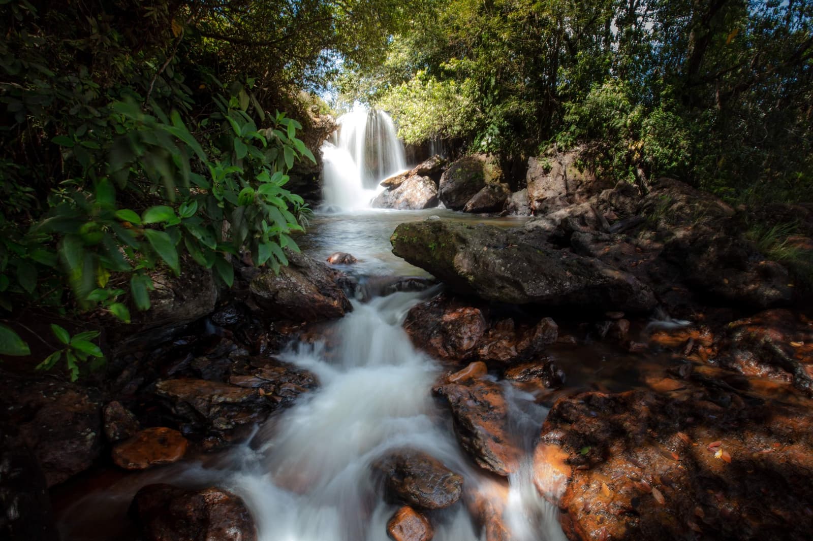 Kaltes Wasser, warme Steine, kein Gedränge. Wer zu Fuß kommt, verdient genau das. Photo: Alberto Andrich Ein seidiger Wasserfall stürzt durch dichten Wald auf moosbedeckte Felsbrocken und speist einen schnell fließenden Bach über rostfarbene Steine auf einer Jalapão-Trekkingroute