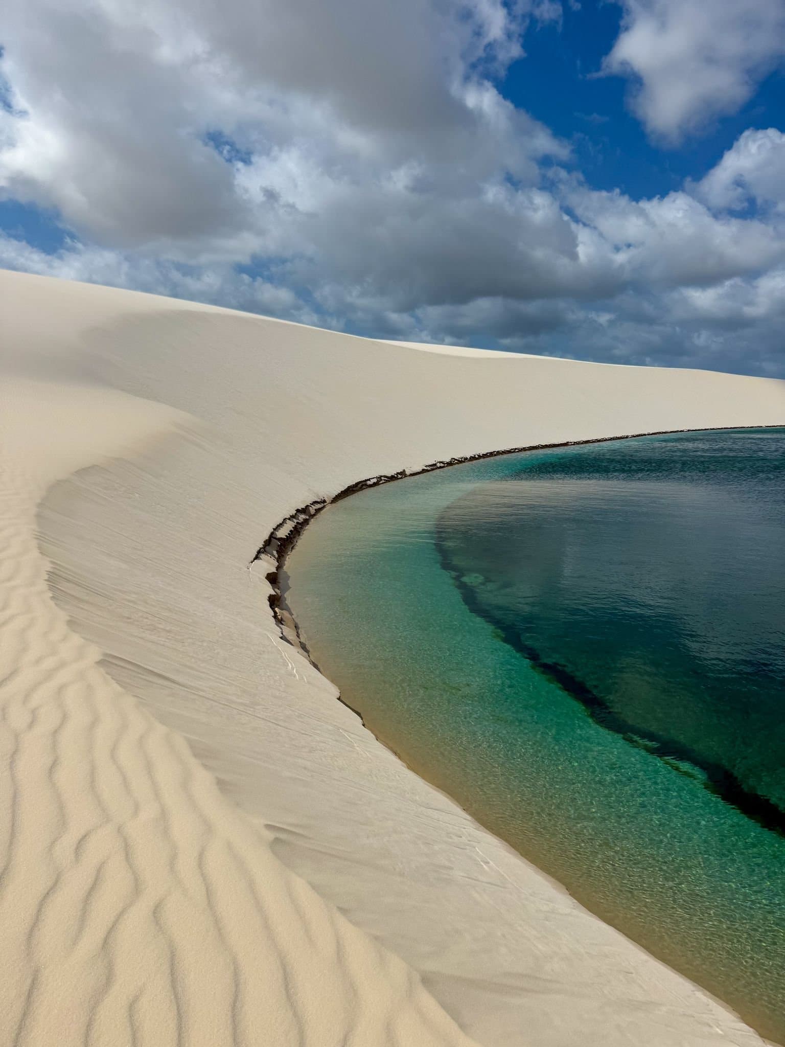 Wüste trifft Wasser, und keiner der beiden weicht zurück. Ein kristallklarer türkisfarbener Lagunenpool, der von makellos weißen Sanddünen unter bewölktem Himmel umschlossen wird – ein Highlight des Lençóis Maranhenses Full Itinerary