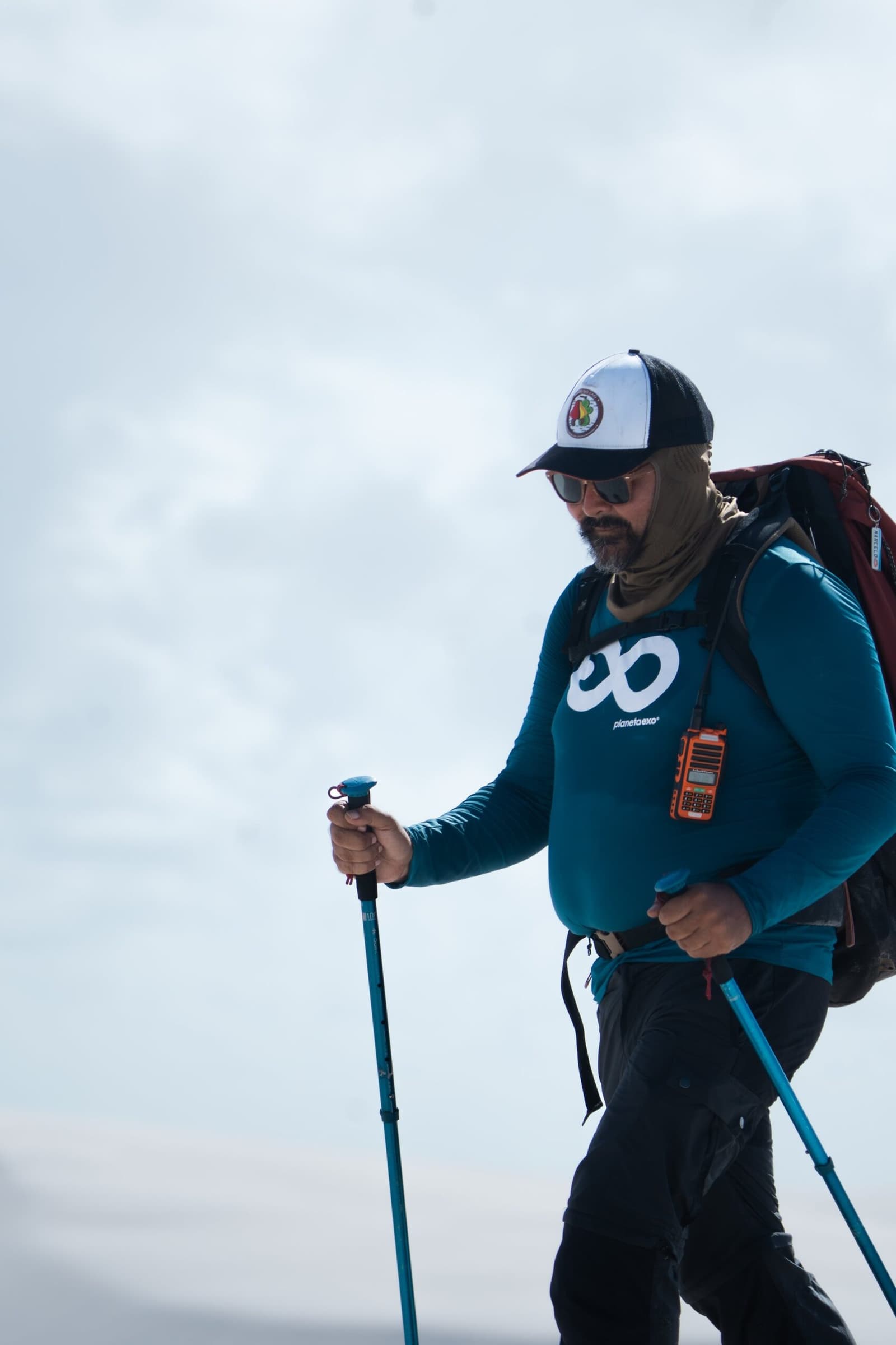 Ausgerüstet für alles, was der nächste Hügel bereithält. Ein PlanetaEXO-Guide in voller Trekking-Ausrüstung mit Wanderstöcken, großem Rucksack und einem Funkgerät am Brustgurt bei der Wanderung durch die Lençóis Maranhenses