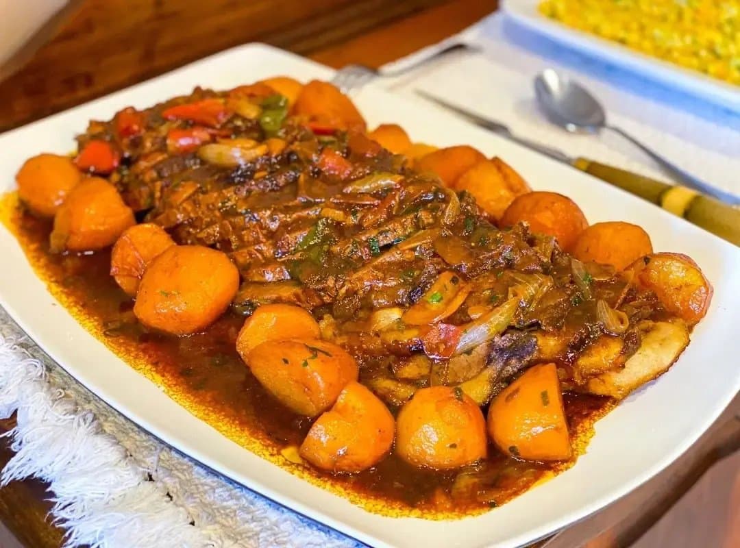 Pantaneiro cooking rewards patience, and this platter makes that obvious. A white serving platter of slow-braised beef in rich dark sauce with roasted potato balls and sautéed peppers and onions, served at a southern pantanal safari lodge