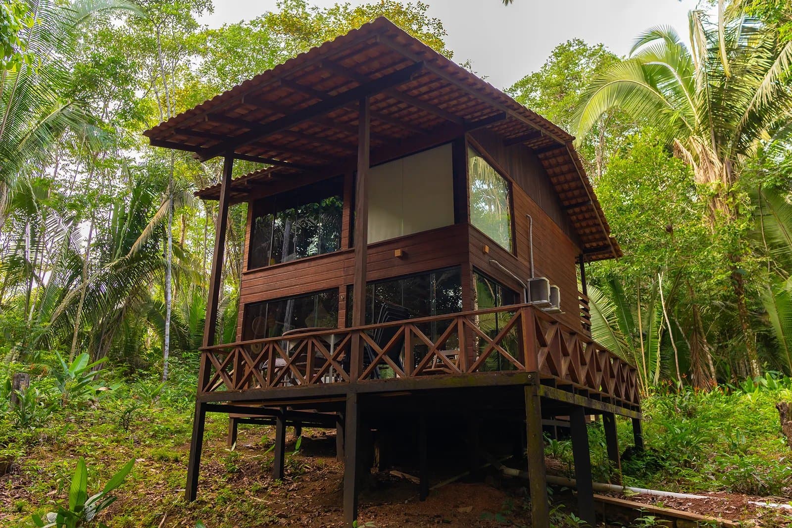 Hochgestellt über den Waldboden, nah genug am Dschungel, um ihn zu hören. Eine zweigeschossige Holzhütte einer Amazon-Boutique-Lodge auf Stelzen mit raumhohen Glasfenstern und einer umlaufenden Veranda, umgeben von dichtem Tropenwald