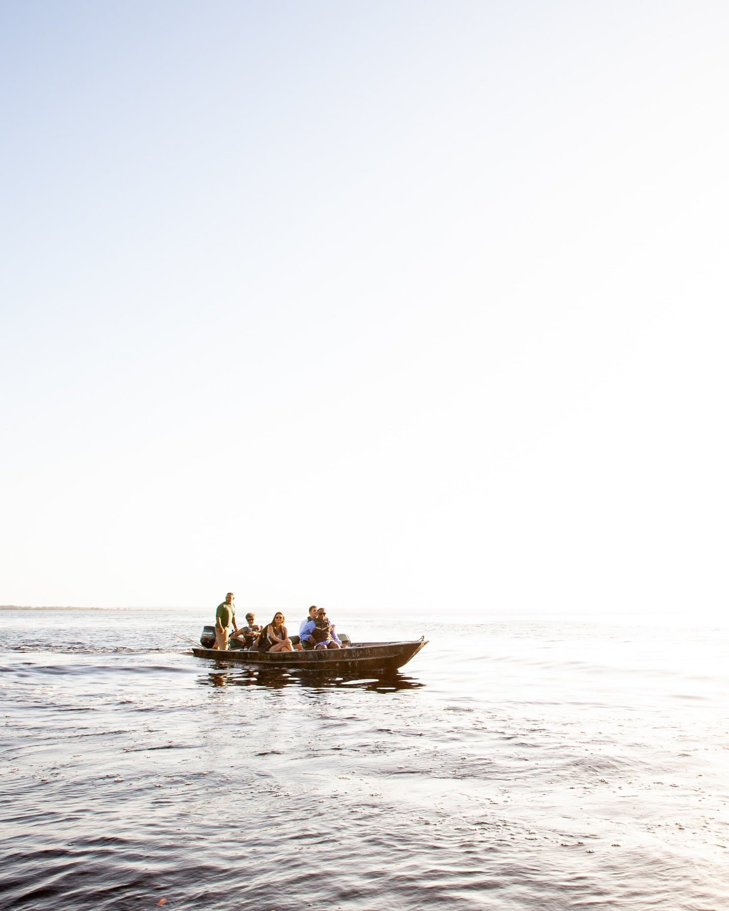 Kein Ufer in Sicht, nur Wasser, Licht und gute Gesellschaft. Eine kleine Reisegruppe sitzt in einem Holzmotorboot auf dem ruhigen, dunklen Wasser des Rio Negro bei einer Amazon-Kreuzfahrt in Brasilien, unter einem weiten, hellen Himmel