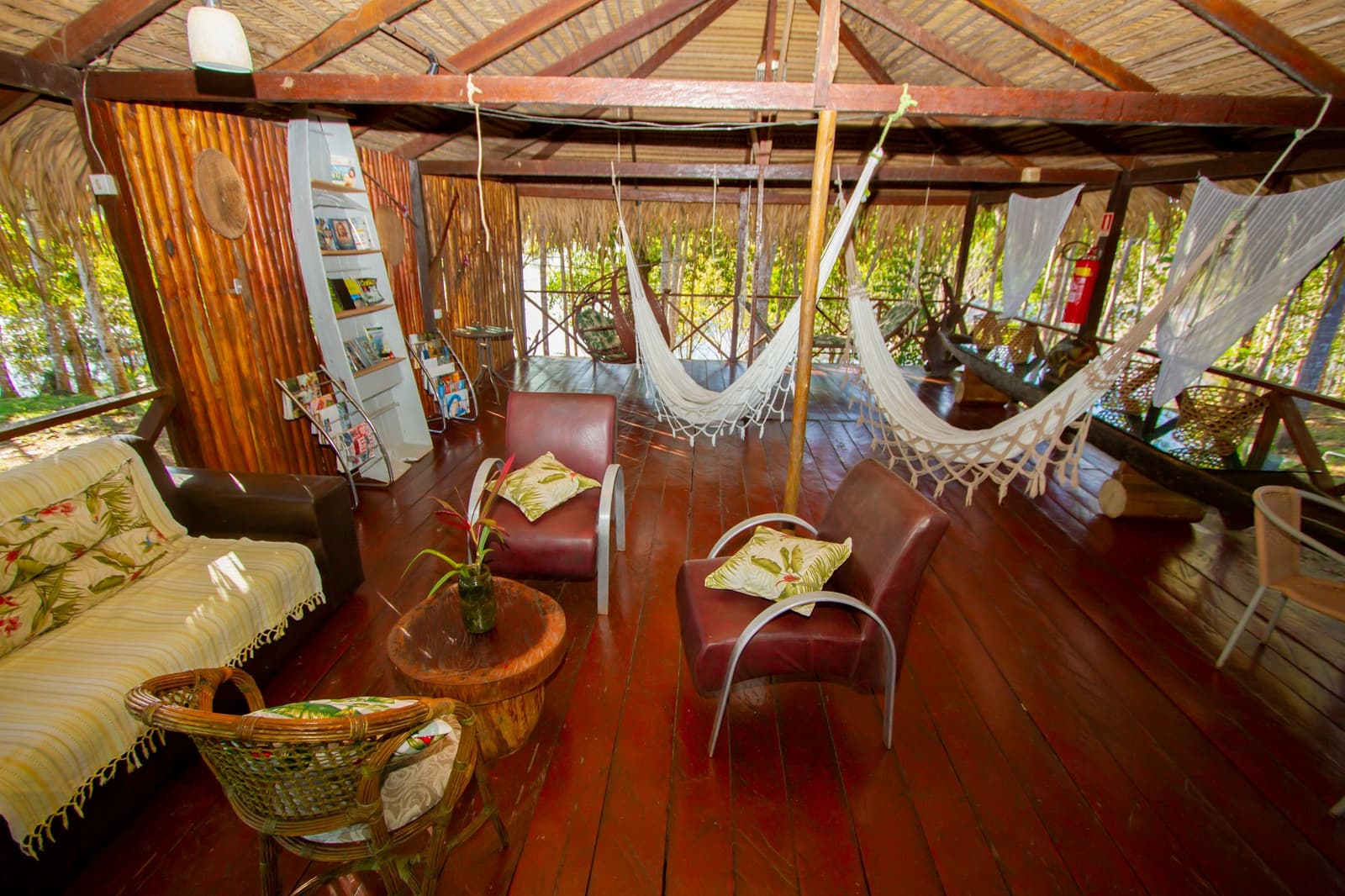 Hängematte aussuchen, Buch schnappen, Regenwald übernimmt den Rest. Offene Gemeinschaftslounge im Amazon Turtle Lodge mit gewebten Hängematten, Ledersesseln und einem polierten Hartholzdeck umgeben von Regenwald