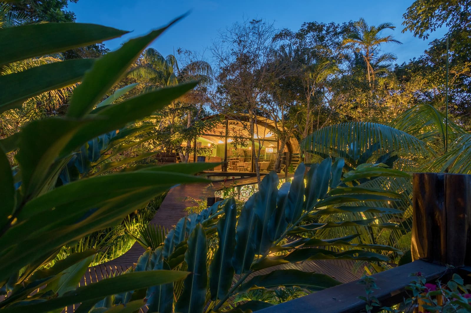 Im Dschungel fängt der Abend erst richtig an. Ein erleuchteter offener Pavillon des Mirante do Gavião in der Abenddämmerung, umrahmt von üppigem tropischem Blattwerk entlang eines Holzstegwegs