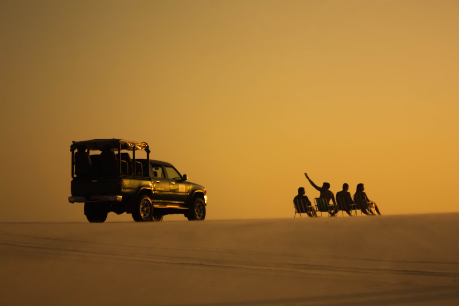 Stühle in den Dünen, kein Plan außer diesem Licht. Vier Reisende sitzen auf Klappstühlen auf einer weiten Düne im goldenen Abendlicht, neben einem Geländewagen im Lençóis Maranhenses