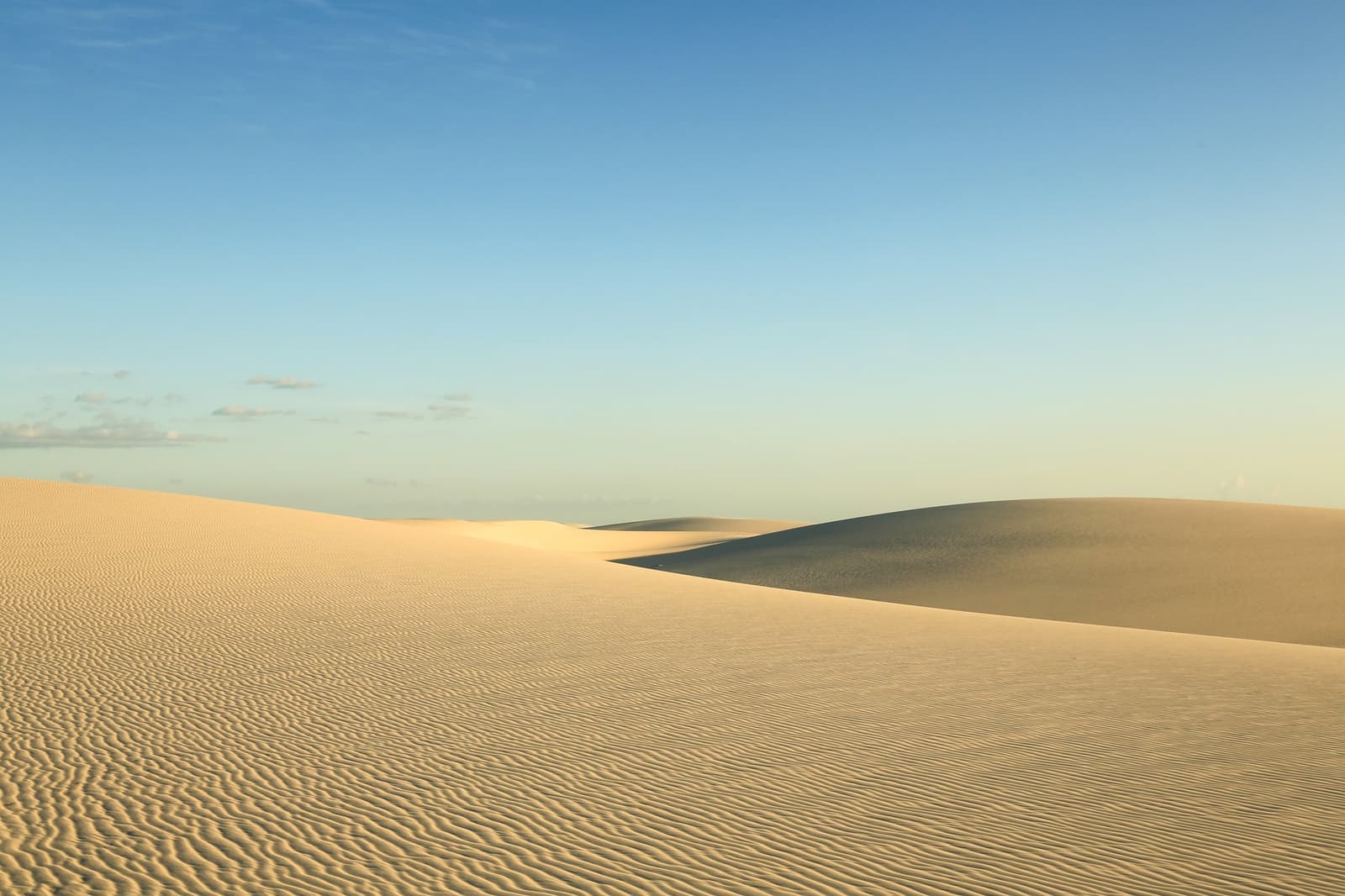 Stille, die man fast hören kann, nur Sand, Wind und Licht. Weite weiße Sanddünen mit windgeformten Oberflächen, die sich unter einem klaren blauen Himmel beim Lençóis-Maranhenses-Trek bis zum Horizont erstrecken