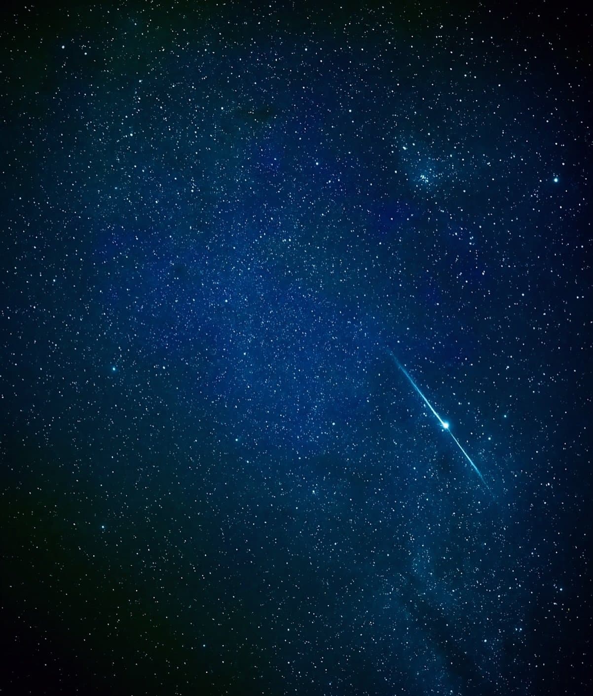 Keine Lichtverschmutzung, kein Stadtlärm, nur das hier. Eine helle Sternschnuppe zieht diagonal über einen tiefblauen, sternenübersäten Nachthimmel, mit Tausenden sichtbarer Sterne der Milchstraße