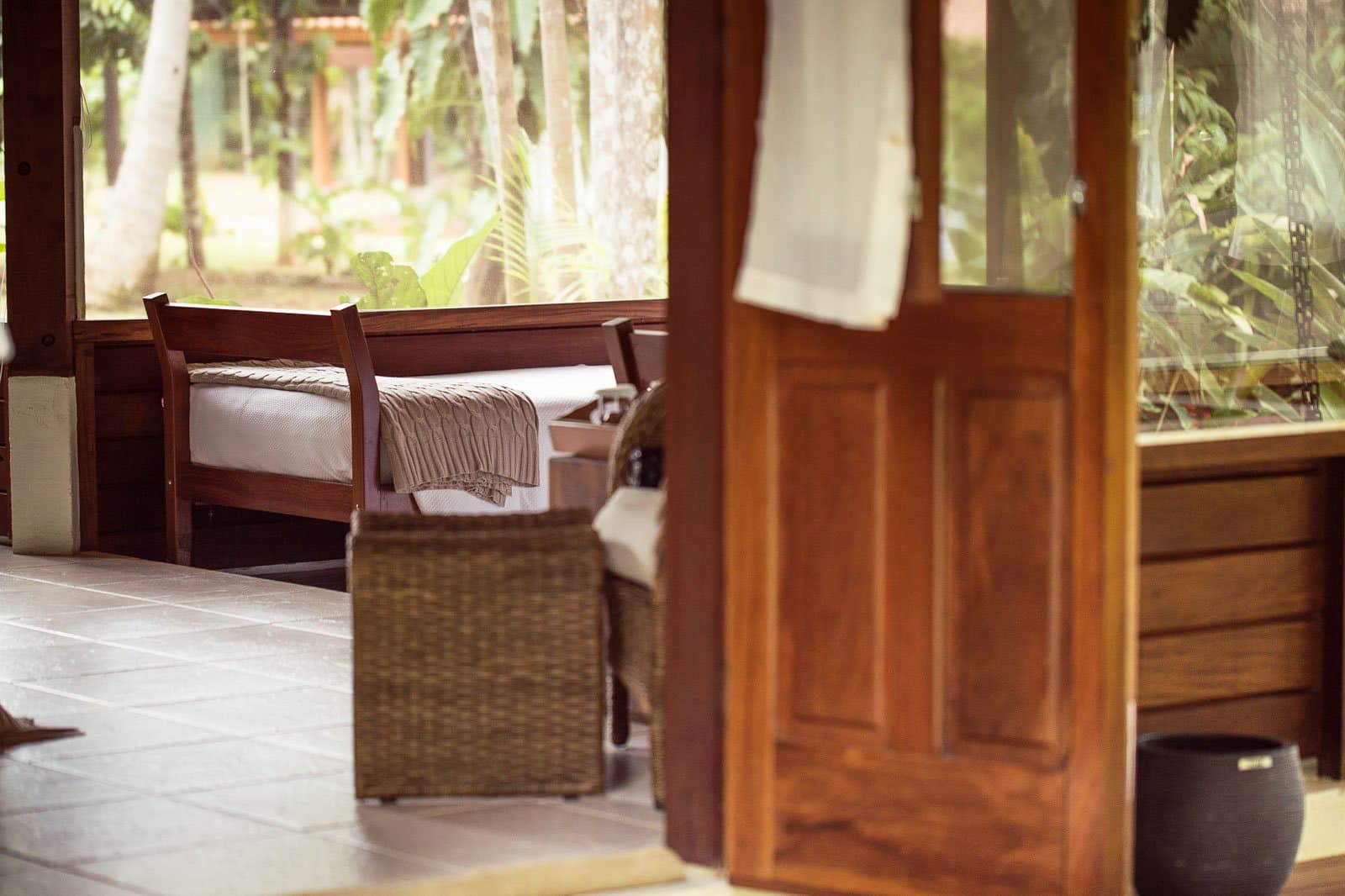 Sobre, chaleureux et calme, tout ce qu'il faut avant le réveil à 5 h du matin. Photo: | SamuelMelim Photography Intérieur d'un bungalow en bois dans un lodge d'observation des oiseaux en Amazonie, avec un lit simple, un jeté en maille, un fauteuil en rotin et des murs ouverts donnant sur la forêt verte