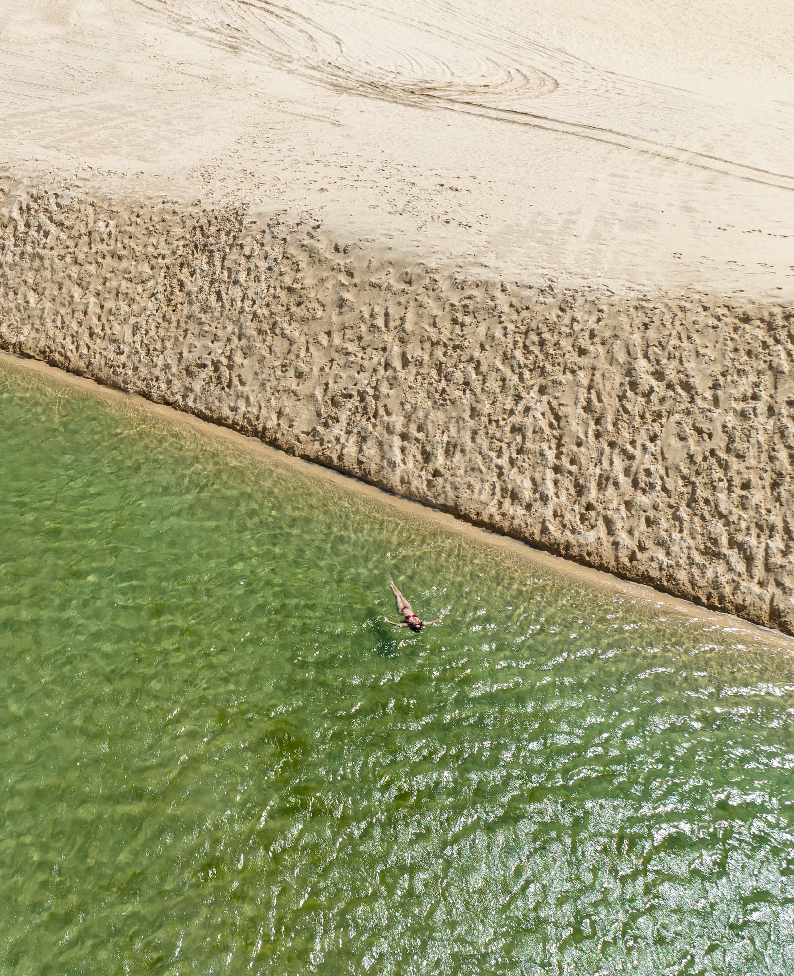 Seul au monde, et ça convient parfaitement. Vue aérienne d'une personne flottant dans une eau verte et claire le long d'un banc de sable texturé lors d'un trek dans les Lençóis Maranhenses