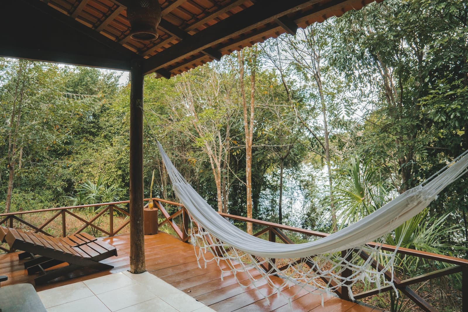 Keine weiteren Pläne für den Nachmittag nötig. Eine weiße Hängematte aus Seil hängt auf einer Hartholzterrasse der Amazon Turtle Lodge, mit einem Holzliegestuhl und üppigem Regenwalddach hinter dem Geländer