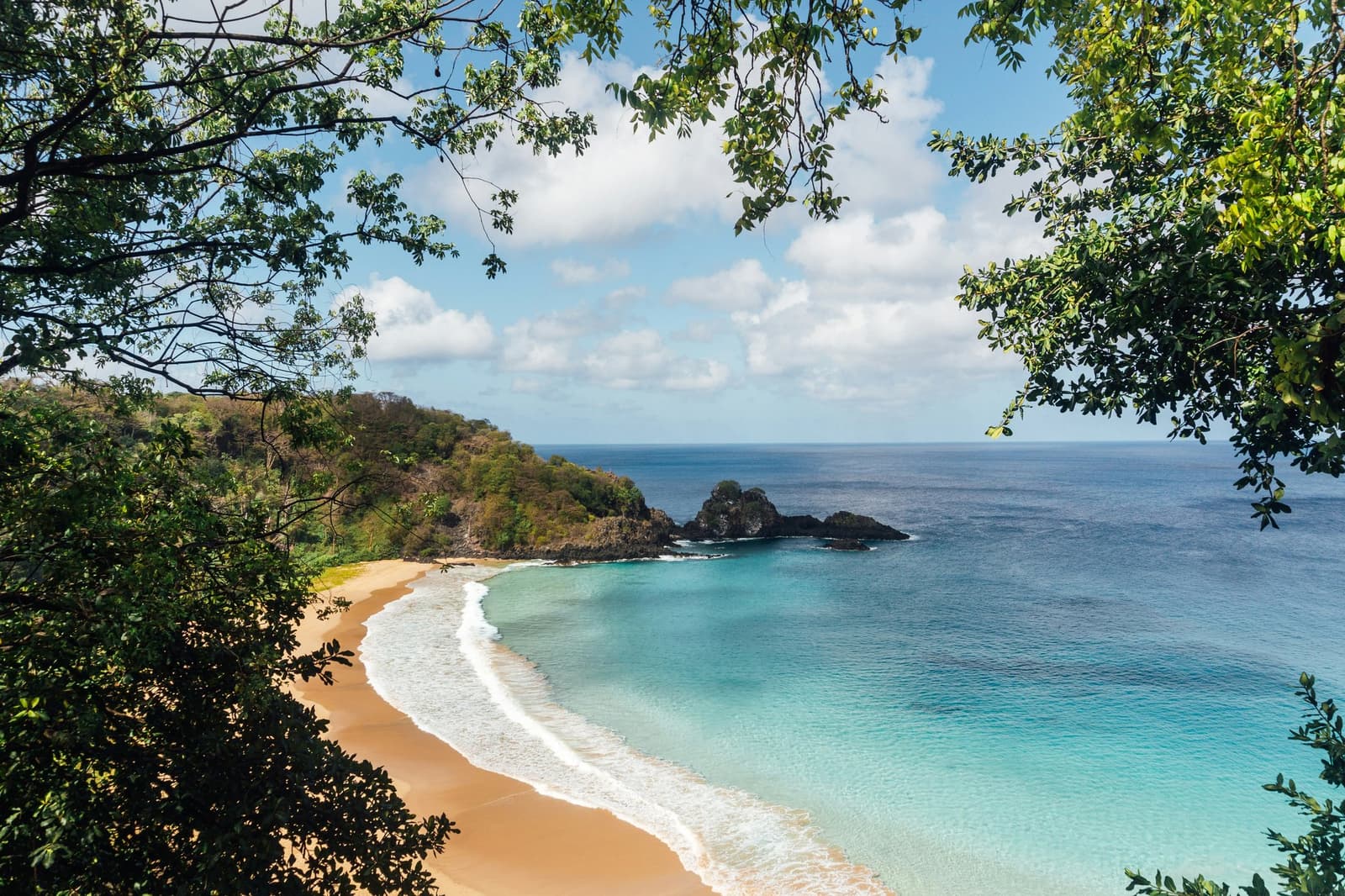 Stille baai, flikkerend turquoise — de eilandkust op zijn puurste. Een afgelegen goudkleurige baai met turquoise water en vulkanische rotsen, omlijst door tropisch groen op Fernando de Noronha