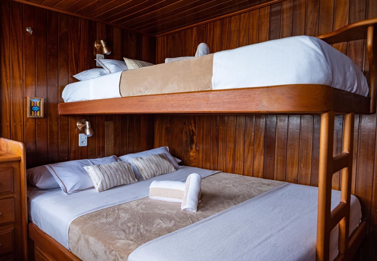 Klein, warm und erstaunlich bequem, der Fluss schaukelt einen in den Schlaf. Eine gepflegte Holzkabine mit Etagenbetten auf einer Amazonas-Kreuzfahrt ab Alter do Chão: unten ein Doppelbett mit weißer und taupefarbener Bettwäsche, oben eine weitere Koje, Messingleseslampen und dunkle Holzverkleidung