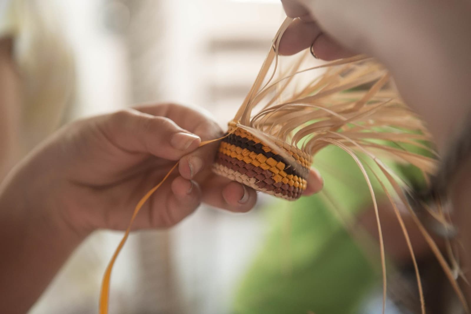 Jeder Streifen ist eine Entscheidung, jede Windung braucht Geduld. Nahaufnahme von Händen, die während eines Amazonas-Flusskreuzfahrt ab Alter do Chão einen kleinen gestreiften Korb aus natürlichen Palmfasern flechten