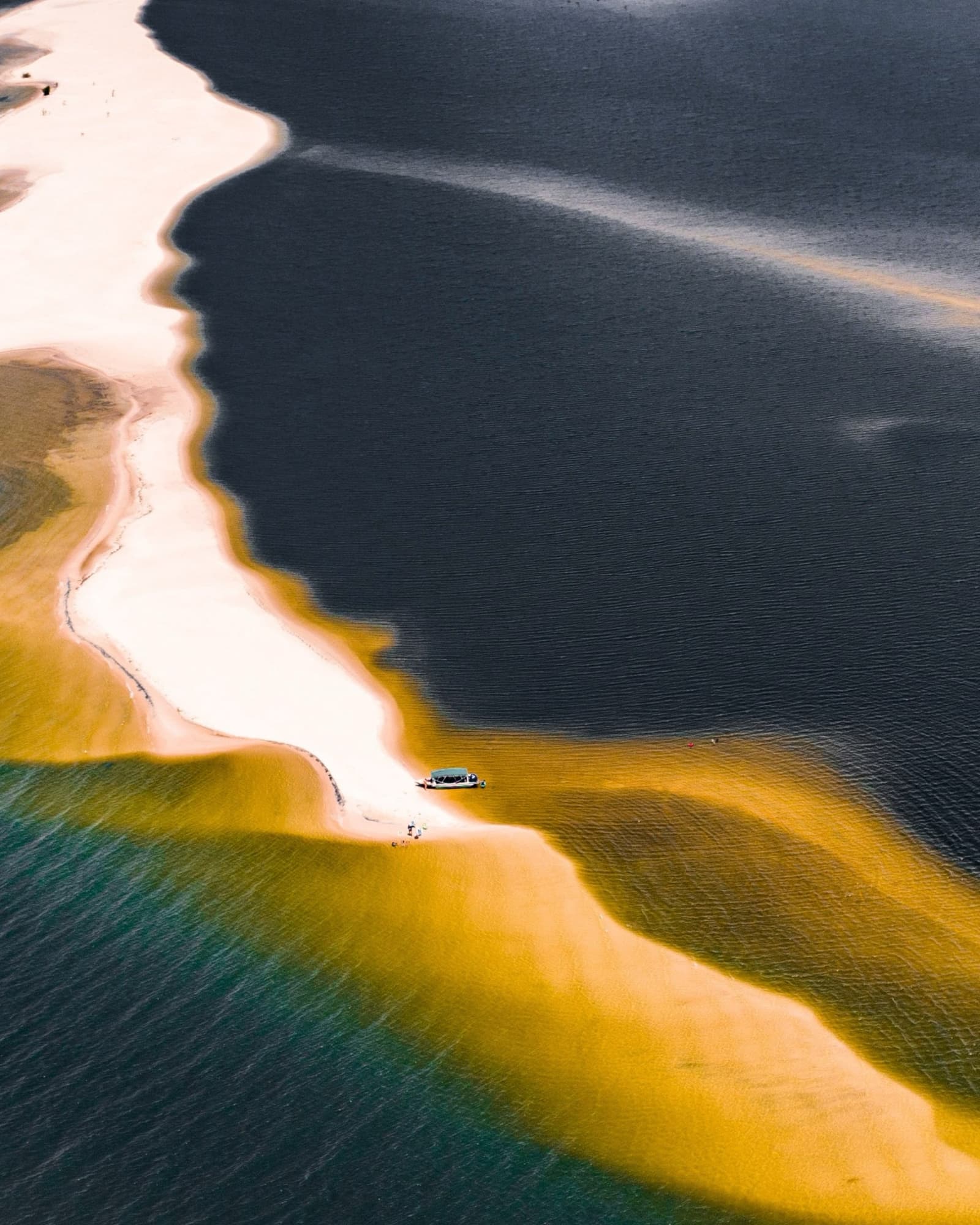 Drei Wasserfarben, ein schmaler Streifen Sand, ein Boot mit dem besten Platz. Luftaufnahme eines kleinen Bootes auf einer geschwungenen weißen Sandbank, wo türkisfarbenes, goldenes und dunkles Flusswasser zusammentreffen – eine Amazonas-Kreuzfahrt ab Alter do Chão
