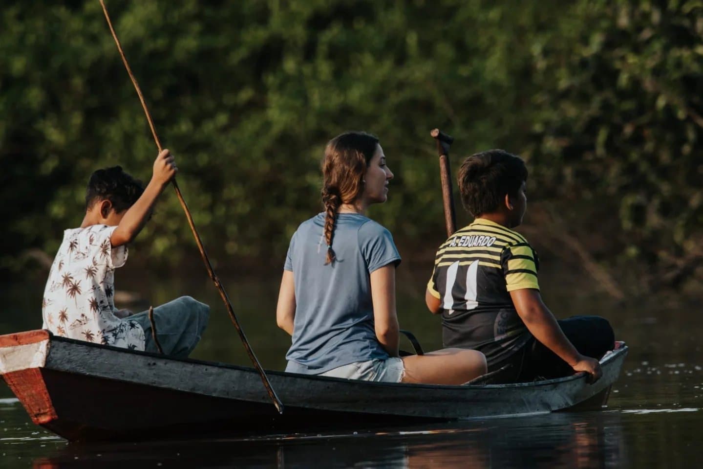 Eux pagaient depuis l'enfance. Elle commence à trouver le rythme. Une femme et deux jeunes locaux pagaient dans un canoë en bois sur une rivière calme en pleine jungle, bordée d'une forêt dense et verdoyante