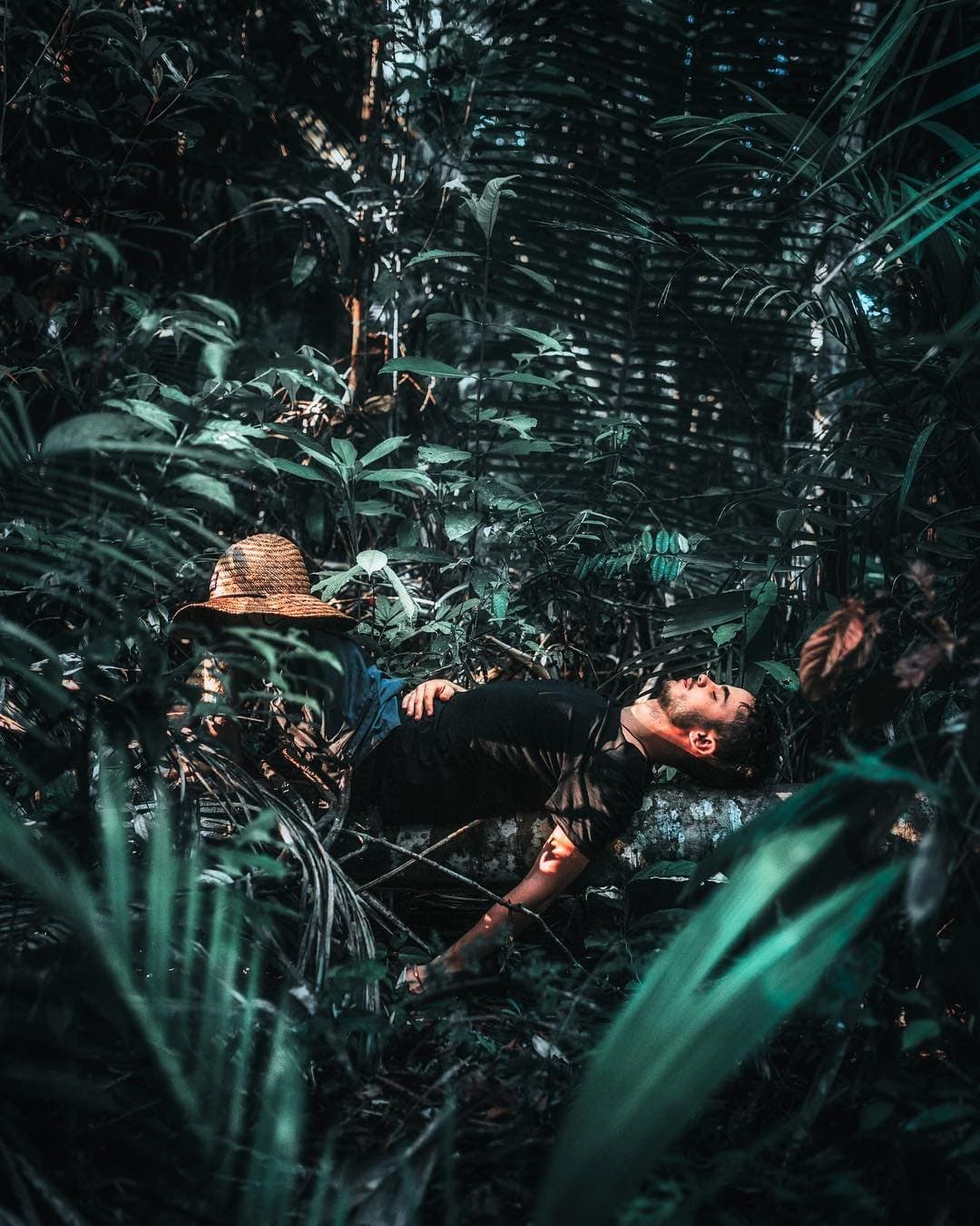 La forêt a sa propre façon de vous forcer à souffler. Un homme allongé sur une bûche moussue au cœur d'une végétation tropicale dense, son chapeau de paille posé à côté, se reposant lors d'un trek de survie en Amazonie