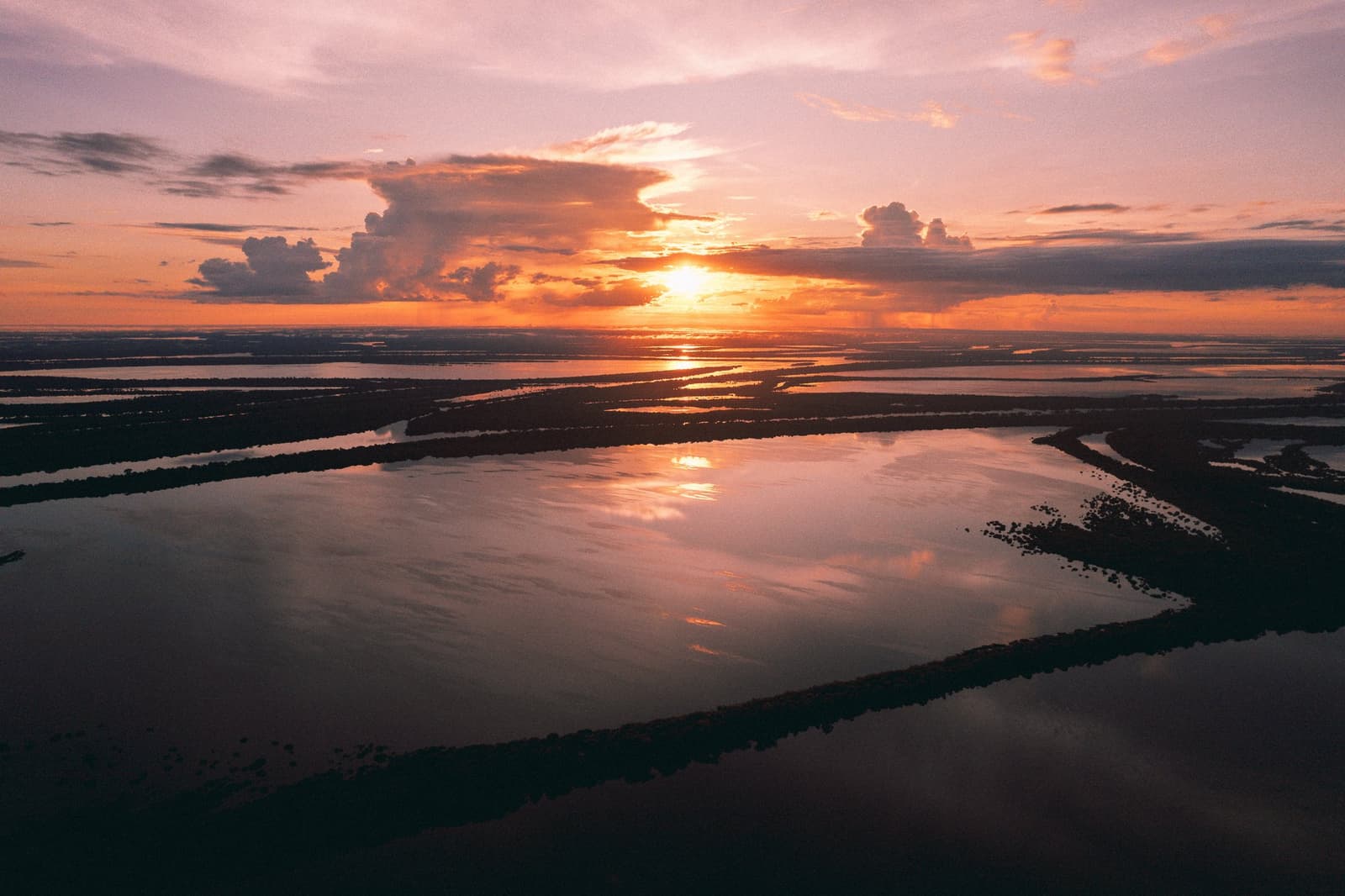 Der Fluss nimmt jede Farbe an, die der Himmel hergibt. Luftaufnahme einer weitläufigen überschwemmten Amazonas-Überschwemmungsebene bei Sonnenuntergang, mit orangenem und rosafarbenem Licht, das sich in den miteinander verbundenen Wasserläufen und dunklen bewaldeten Inseln spiegelt, in der Nähe der Anavilhanas Jungle Lodge Brasilien