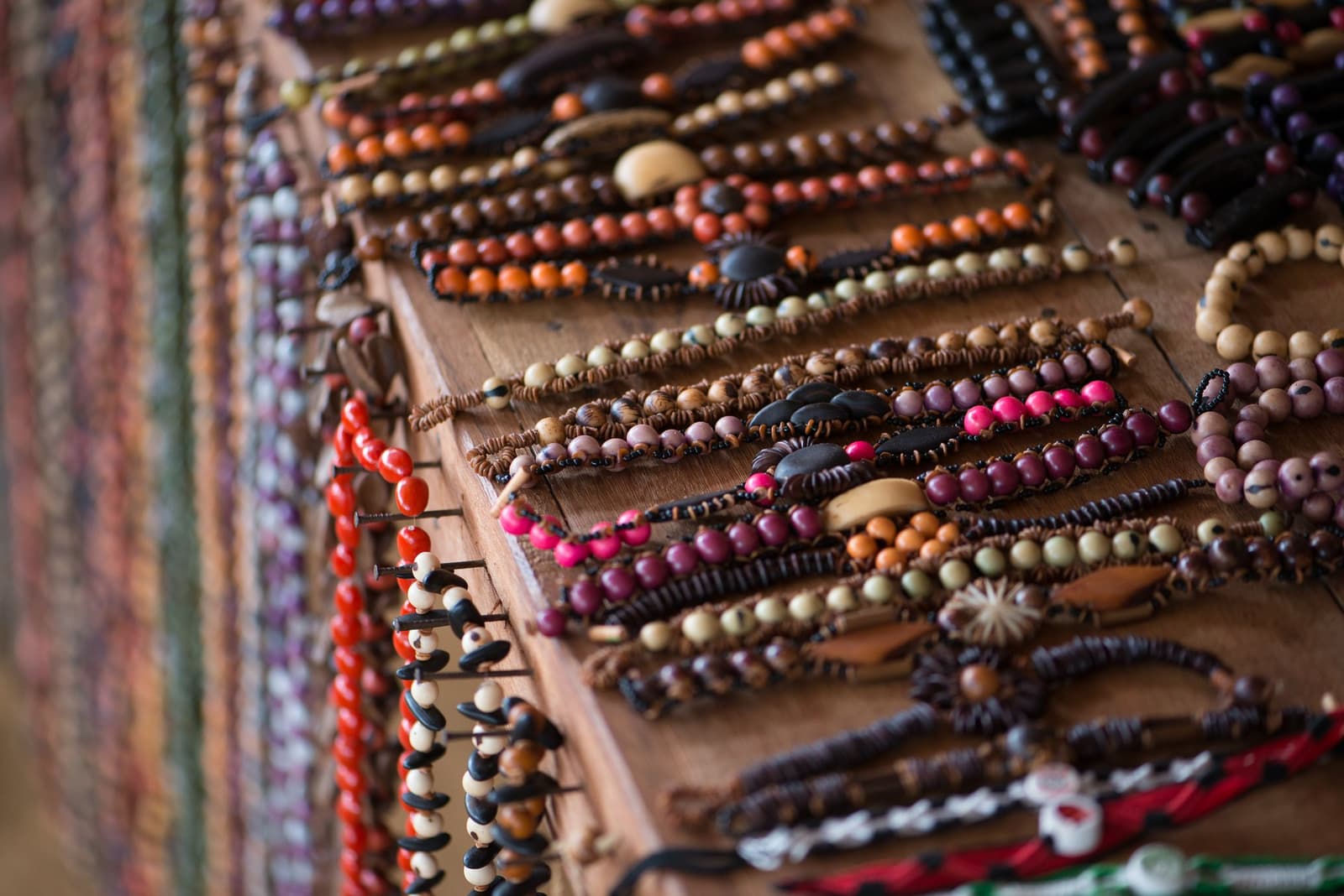 Kleine Samen, viel Können, eine gute Erinnerung zum Mitnehmen. Reihen handgefertigter Armbänder aus bunten Naturkernen und Holzperlen auf einem Holzbrett, hergestellt von einer Flussgemeinde nahe der Anavilhanas Jungle Lodge Brasilien