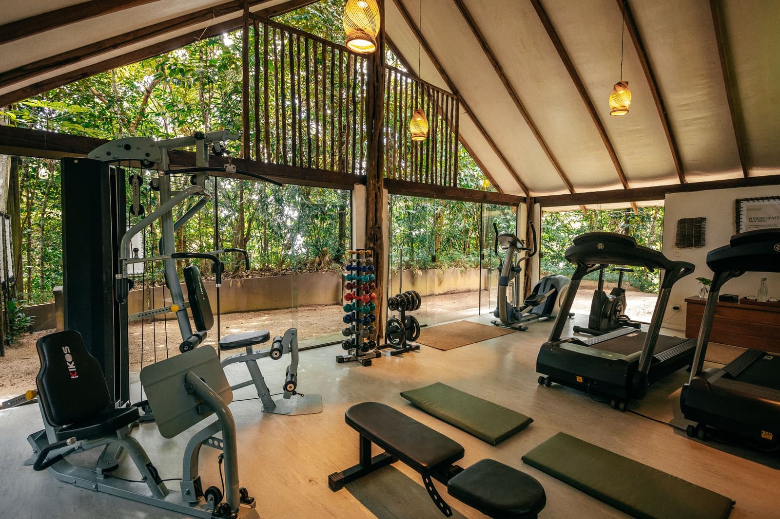 Trainieren mit Blick in den Regenwald, das motiviert anders. Offenes Fitnesscenter der Anavilhanas Jungle Lodge in Brasilien mit Kraftgeräten, Laufbändern, Freihanteln und Yogamatten unter einem Zeltdach, umgeben von tropischem Regenwald hinter Glaswänden