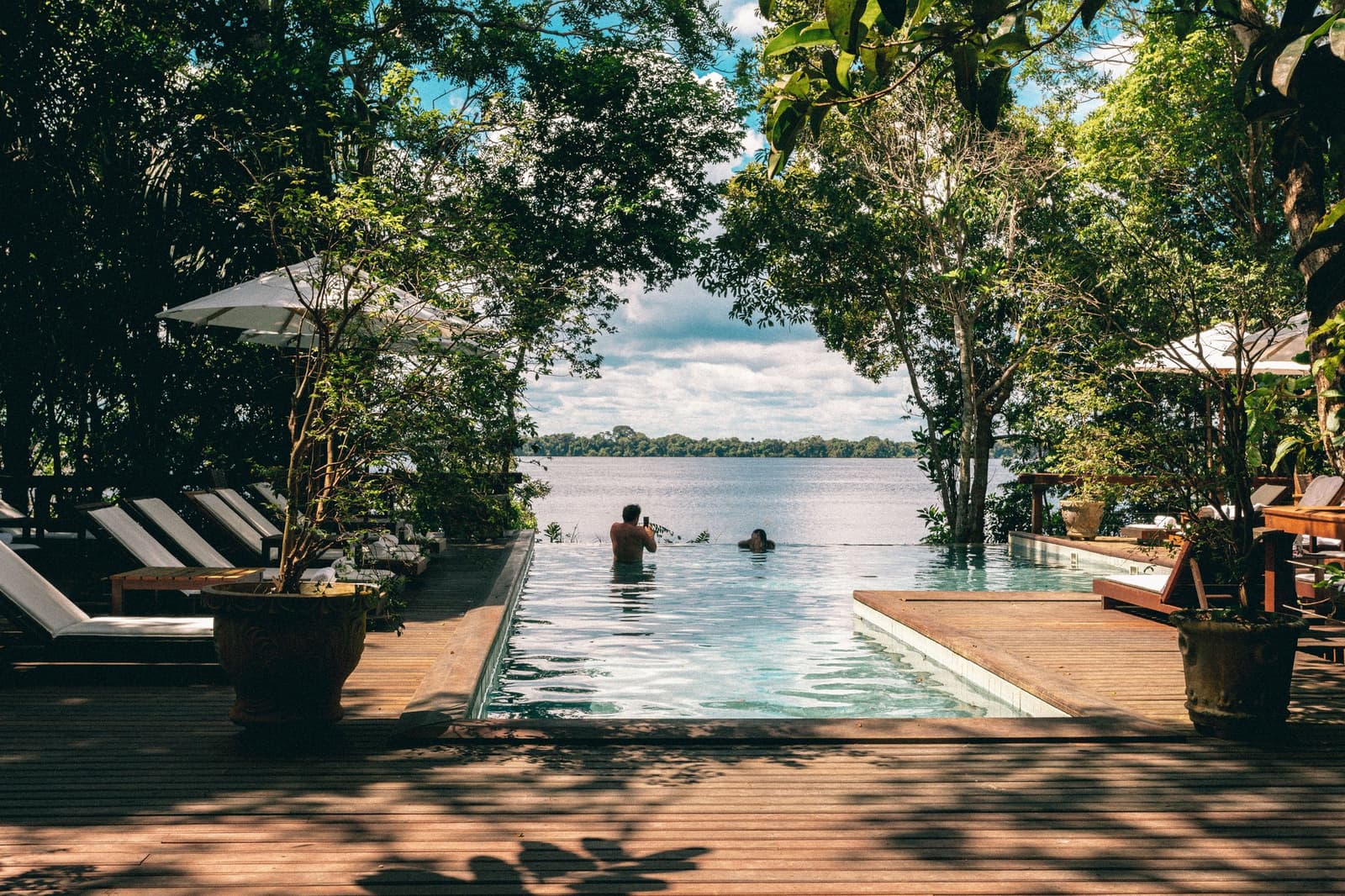 Pool oder Fluss? Hier verschwimmt die Grenze ganz bewusst. Zwei Gäste schwimmen im Infinity-Pool der Anavilhanas Jungle Lodge Brazil, umrahmt von dichtem Regenwald und dem weiten Rio Negro im Hintergrund