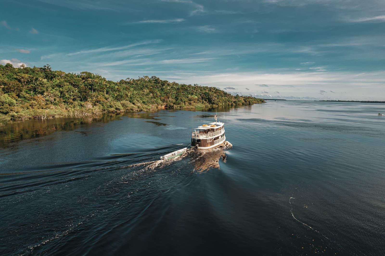 Das schwimmende Zuhause für die nächsten Tage, der Fluss zeigt gleich, was er kann. Ein zweistöckiges Holzboot fährt auf dem dunklen Wasser des Rio Negro entlang dichtem Amazonas-Regenwald bei einer Tagesexpedition des Anavilhanas Jungle Lodge Brazil