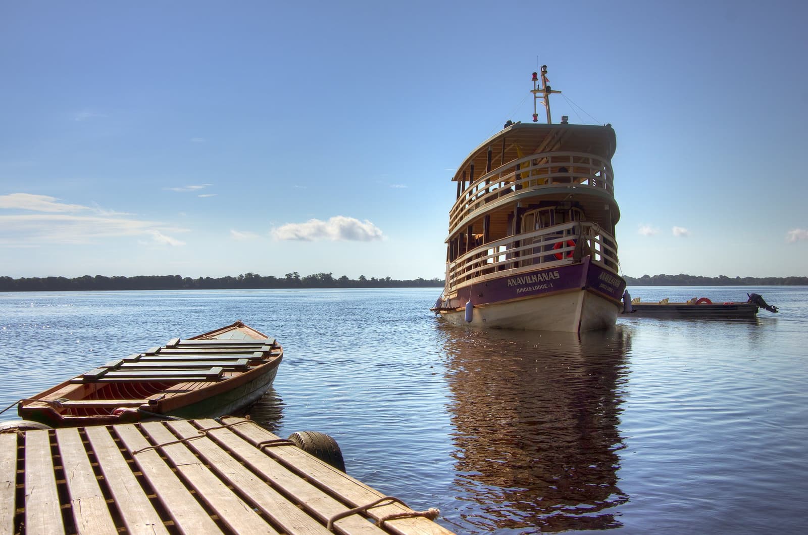 Von hier aus geht es los, das Schiff wartet, der Fluss auch. Das Flussboot der Anavilhanas Jungle Lodge Brasilien liegt auf dem ruhigen schwarzen Wasser des Rio Negro, vom hölzernen Anlegesteg aus gesehen mit einem traditionellen Holzkanu im Vordergrund
