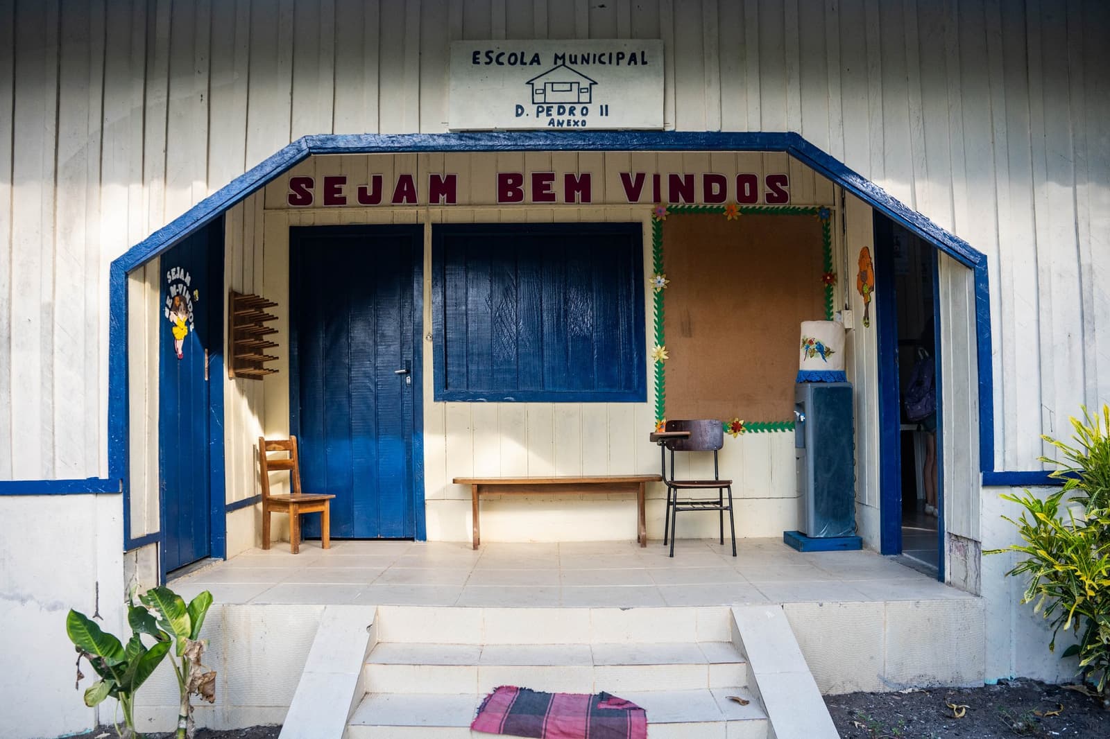 Willkommen heißt es hier wirklich so, in Rot und ohne Ironie. Eingang der Escola Municipal D. Pedro II, einer weißen Holzschule mit blauem Rahmen und dem Willkommensschild 'Sejam Bem Vindos' in einer Flussgemeinde am Amazonas