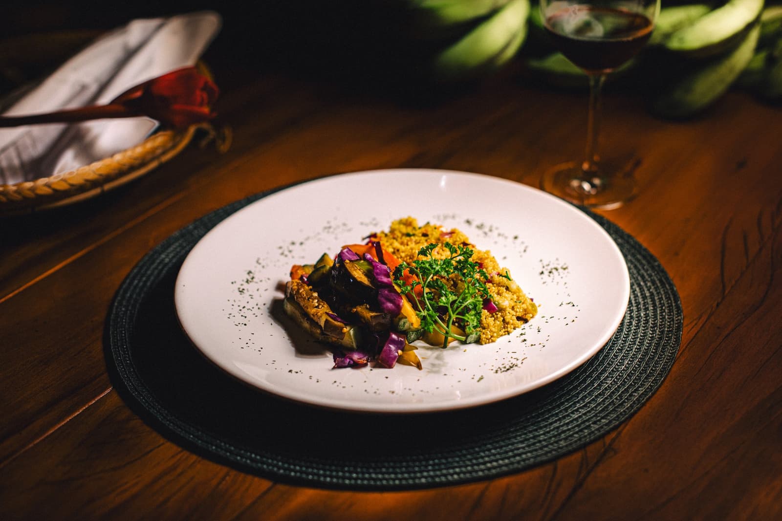 Frisches Gemüse, goldener Couscous und ein Glas Rotwein, der Abend im Dschungel hat Stil. Ein angerichtetes Abendessen in der Anavilhanas Jungle Lodge mit geröstetem Gemüse, goldenem Couscous und frischen Kräutern auf einem weißen Teller, im Hintergrund ein Glas Rotwein
