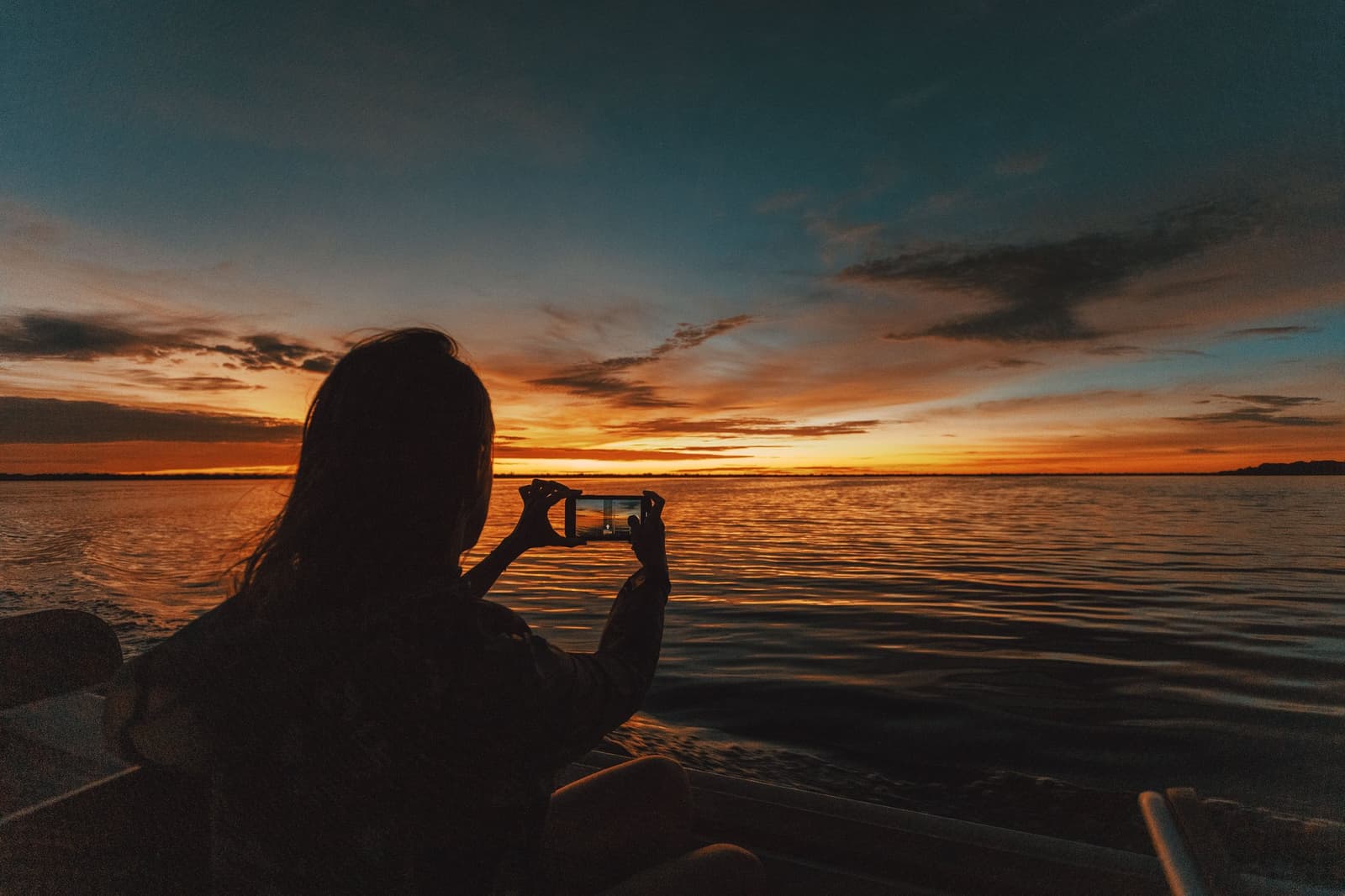 Manche Abende am Amazonas lassen sich einfach nicht in einem Foto fassen. Silhouette einer Reisenden auf einem Boot beim Fotografieren des flammenden Sonnenuntergangs über dem breiten Fluss in der Anavilhanas Jungle Lodge Brasilien