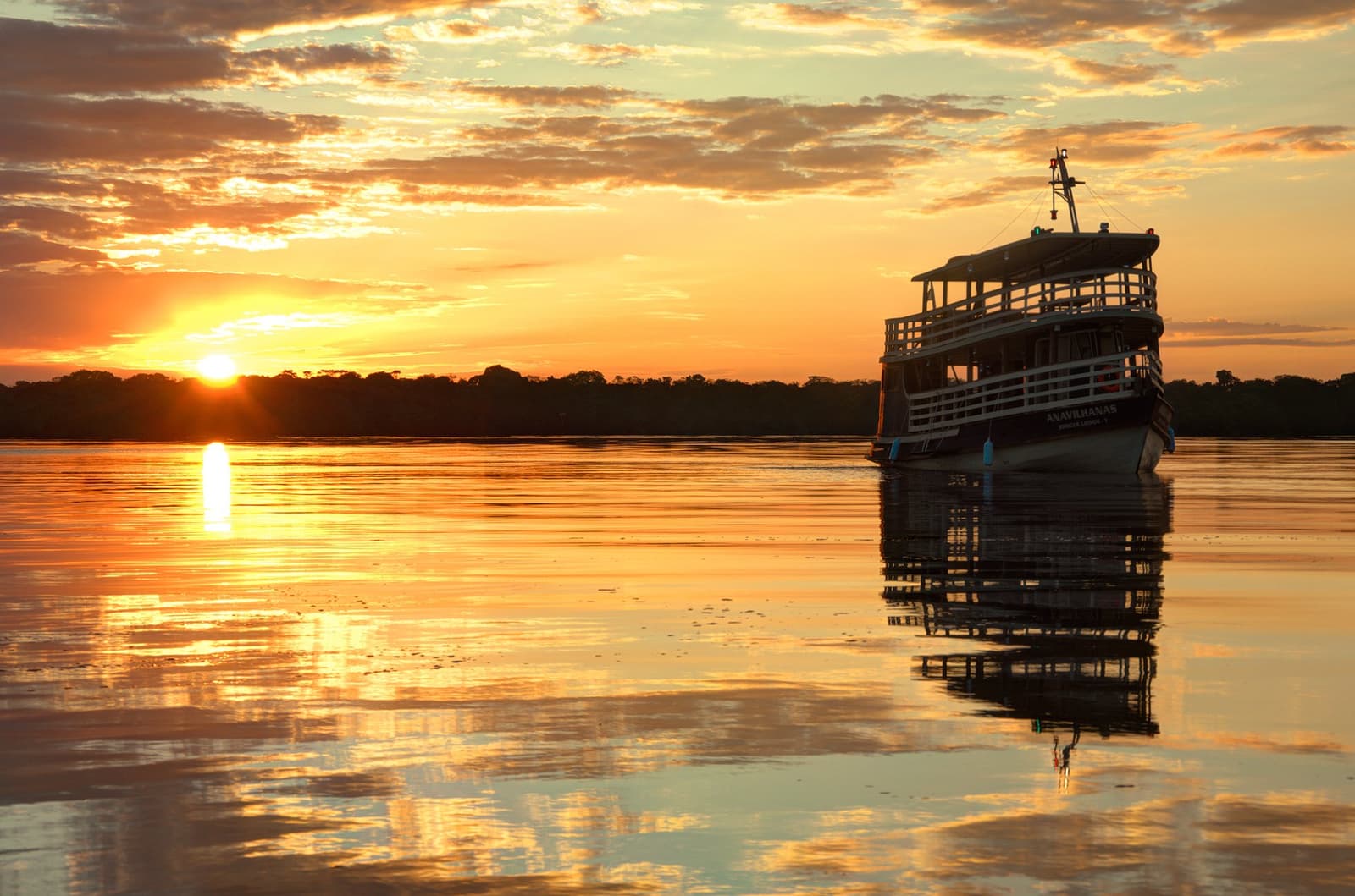 Wenn der Fluss gold wird, braucht man keine weiteren Pläne. Das Expeditionsboot der Anavilhanas Jungle Lodge Brazil liegt auf dem spiegelglatten Rio Negro unter einem glutroten Sonnenuntergang, perfekt im stillen Wasser gespiegelt